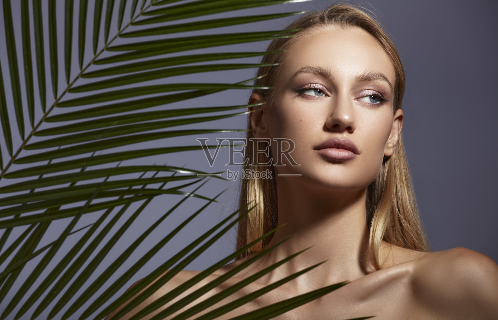 一个美丽的年轻女子的肖像在绿色的棕榈叶后面。照片摄影图片