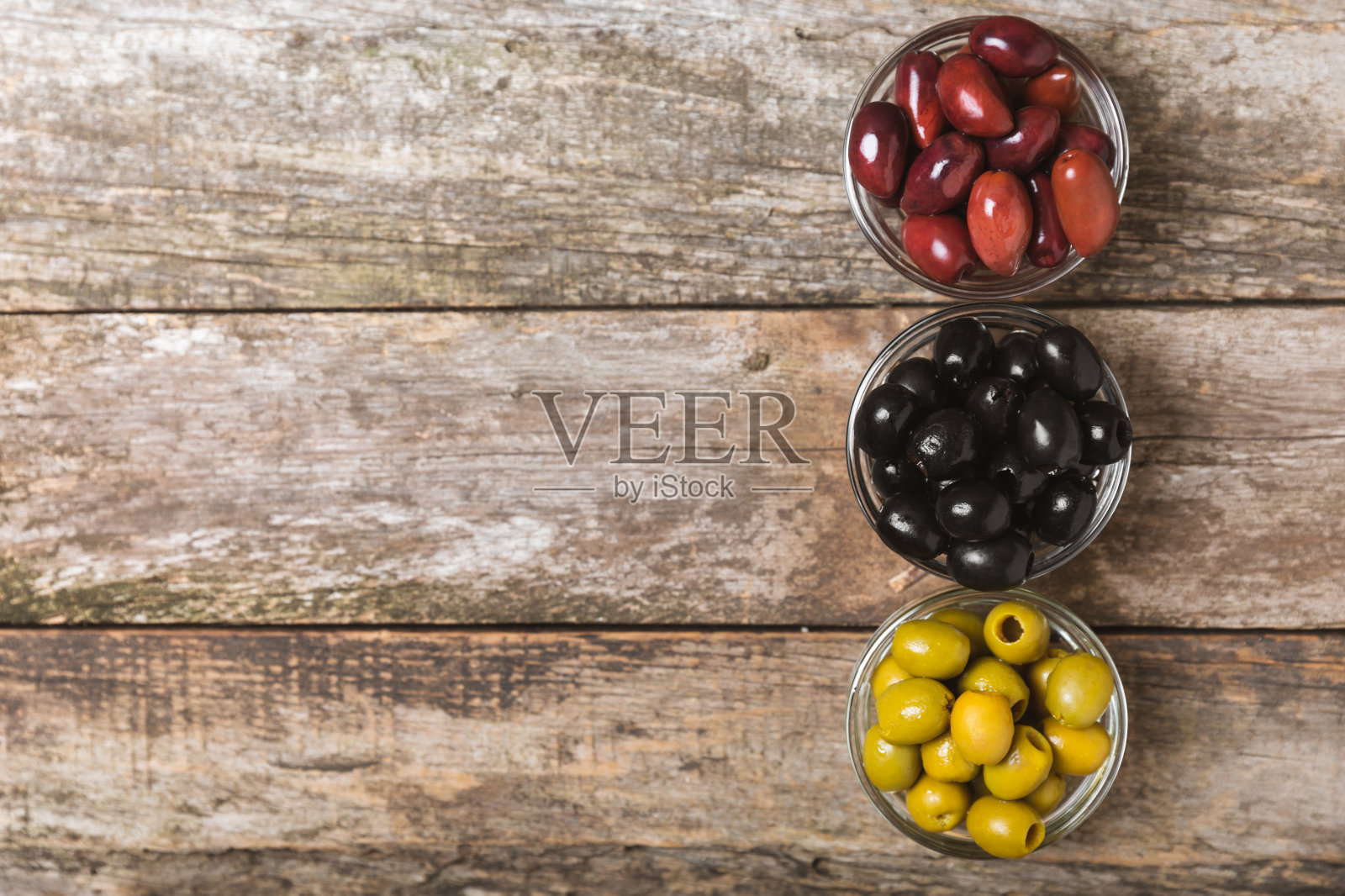 绿色，黑色和红色橄榄纹理的背景。碗里装着各式各样的橄榄，还有配着新鲜橄榄叶的橄榄油。副本的空间。放文字的地方。地中海食物。素食主义者。照片摄影图片