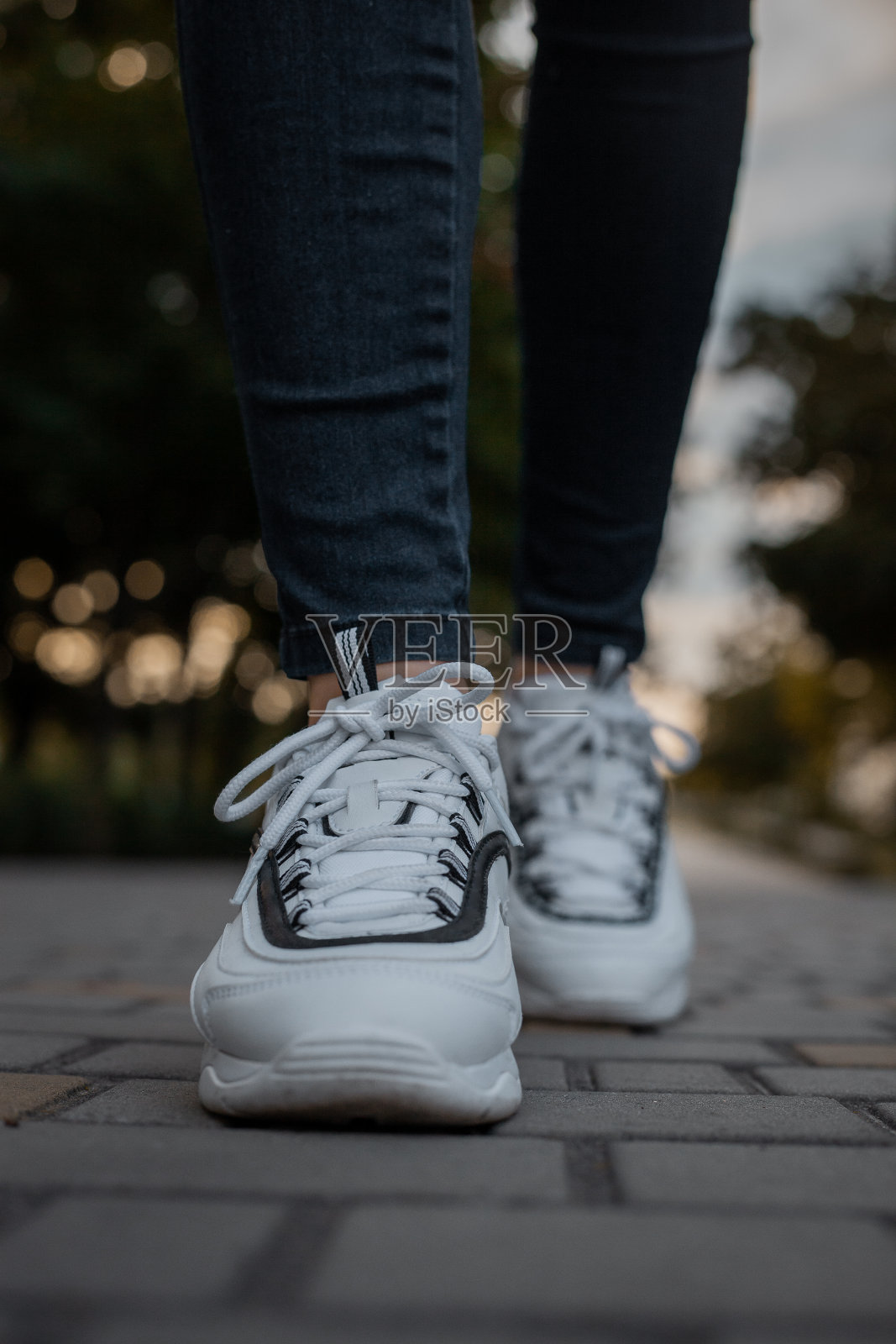 街上一个穿黑色牛仔裤的女孩脚上穿着白色运动鞋照片摄影图片