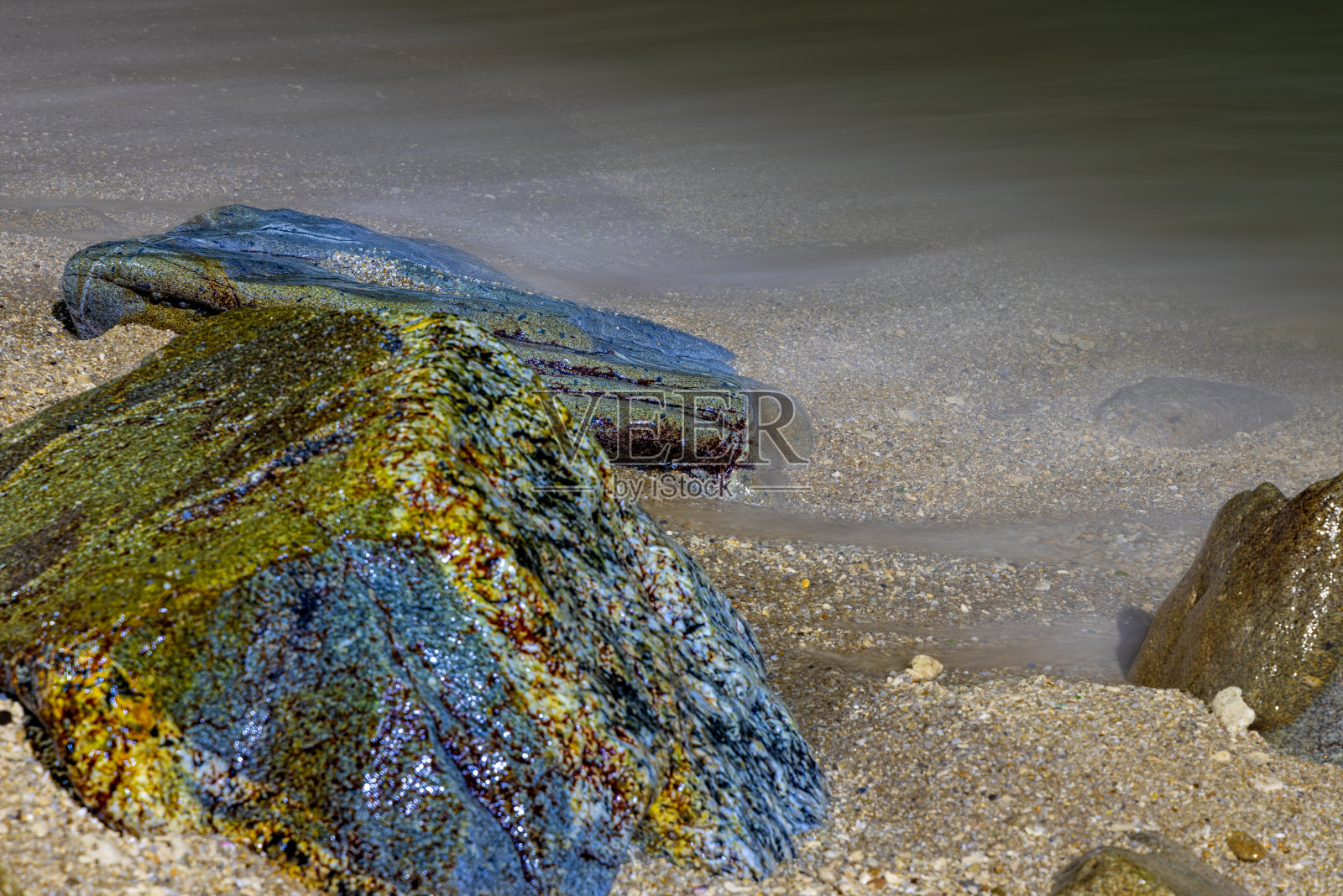 在泰国普吉岛芭东海滩上，长时间暴露在色彩斑斓的夜晚，海浪冲击着岩石照片摄影图片