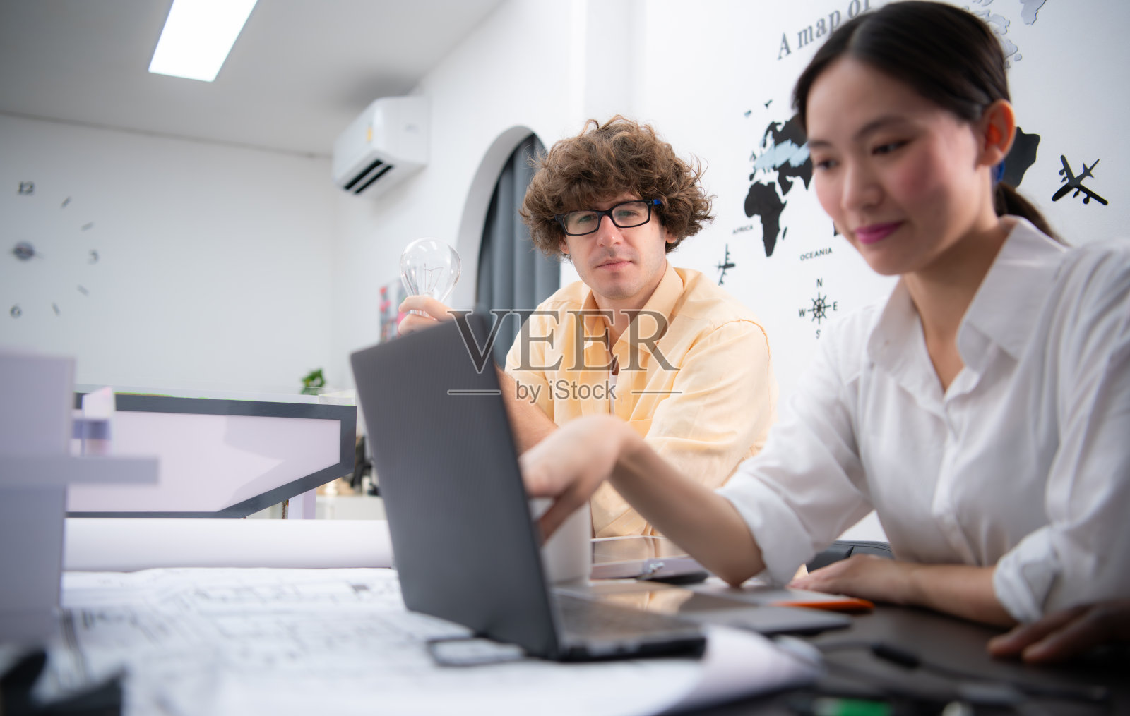 多民族的建筑师和设计师团队正在讨论一个新项目，他带着一个不应该在建筑物中使用的灯泡，因为它既不节能，也不环保。照片摄影图片