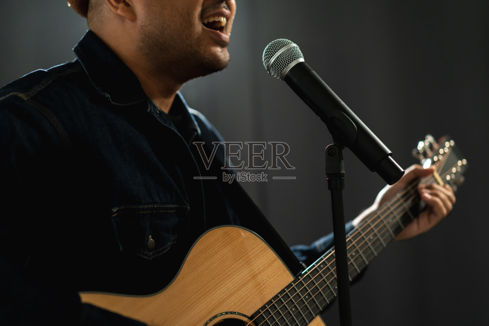 有魅力的歌手男子在舞台上唱着音乐，弹着吉他，聚光灯穿过音乐会的黑暗。音乐家在大厅里用灯光和烟雾现场表演。照片摄影图片