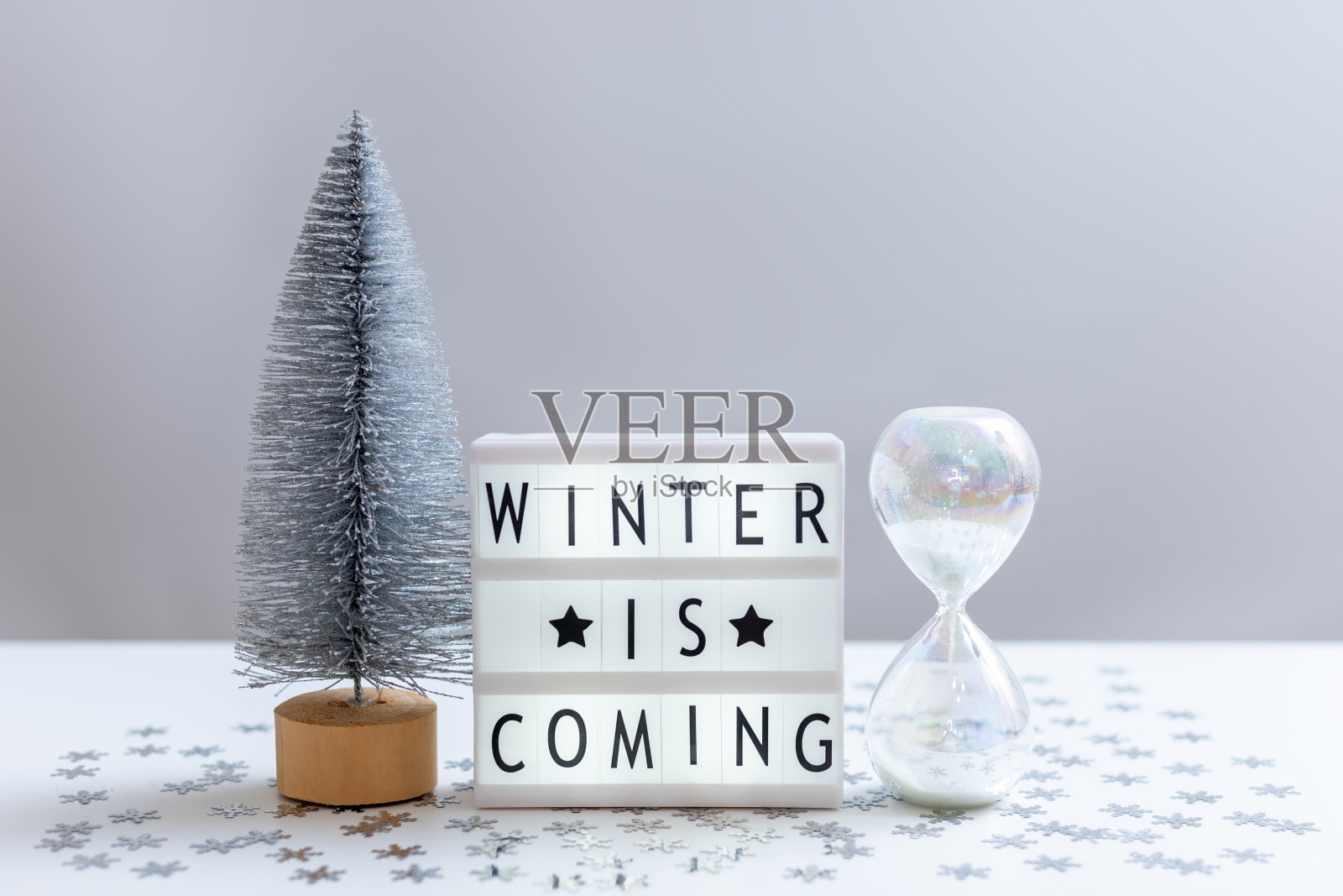 静物画有一棵银色的圣诞树，一个玻璃沙漏和一个灯箱，上面写着“冬天来了”照片摄影图片