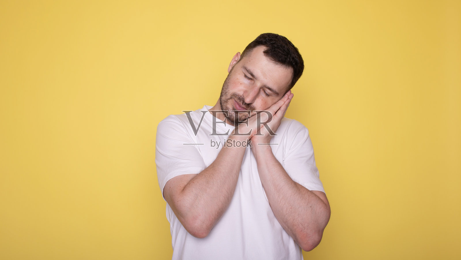 白人男子在黄色孤立的背景下睡觉，做梦，双手合在一起，闭着眼睛微笑。照片摄影图片
