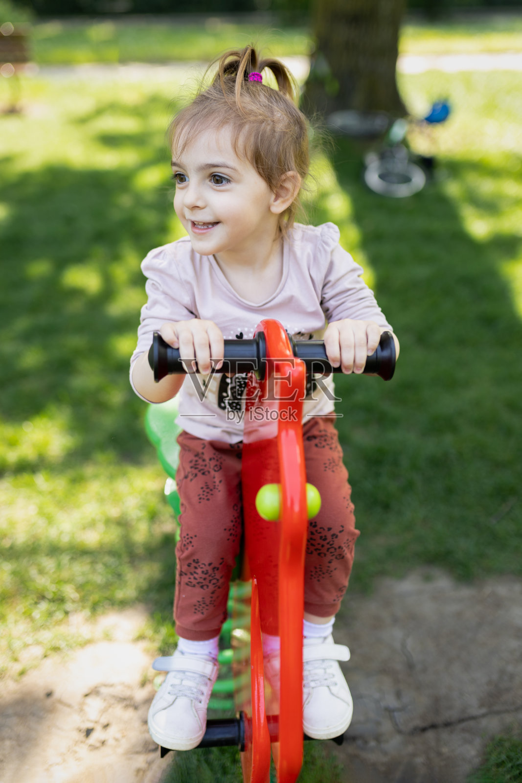 年轻快乐的女孩在公园里骑着摇椅。照片摄影图片