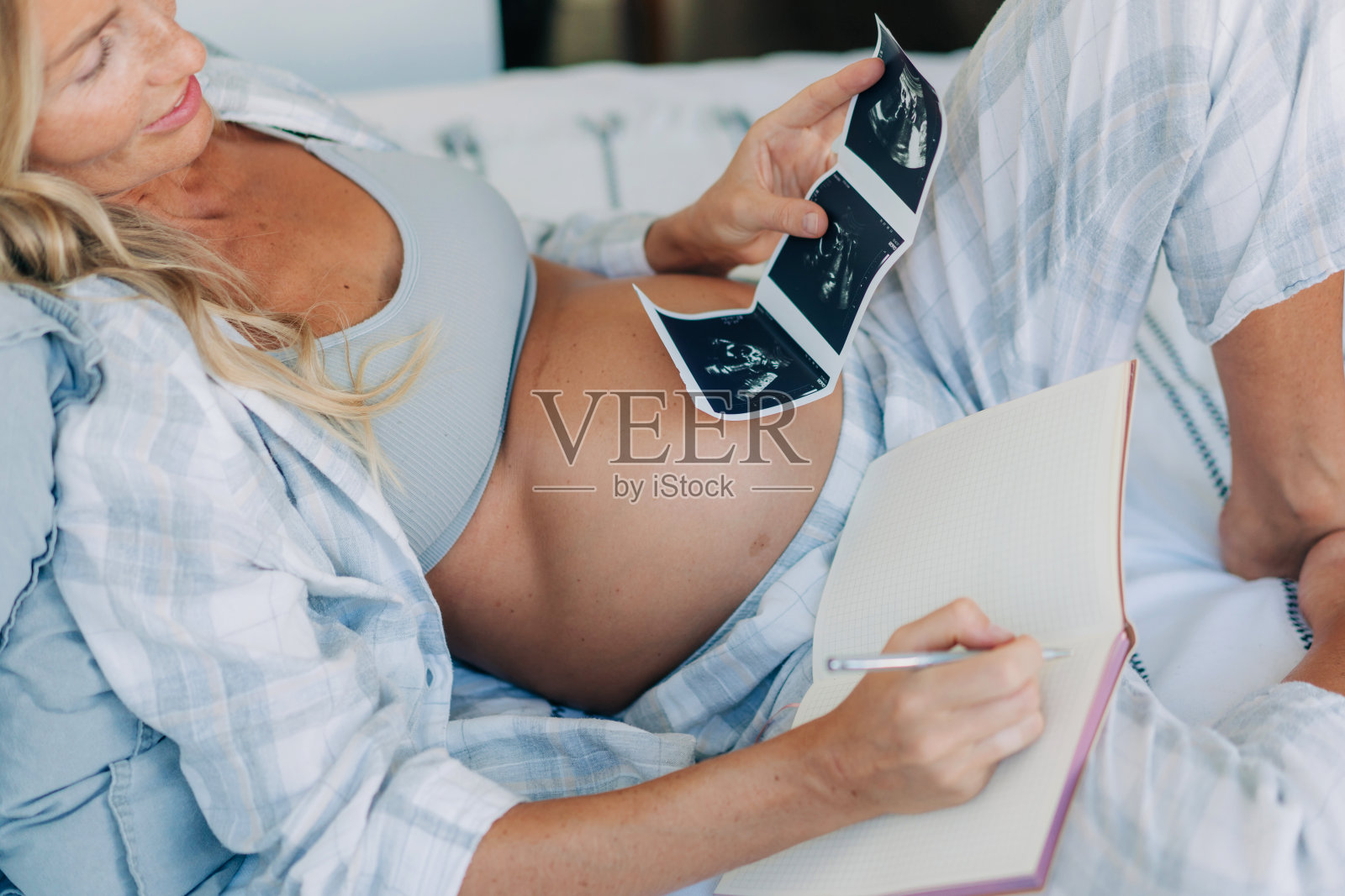 一位年轻的孕妇在笔记本上记录超声检查结果。照片摄影图片