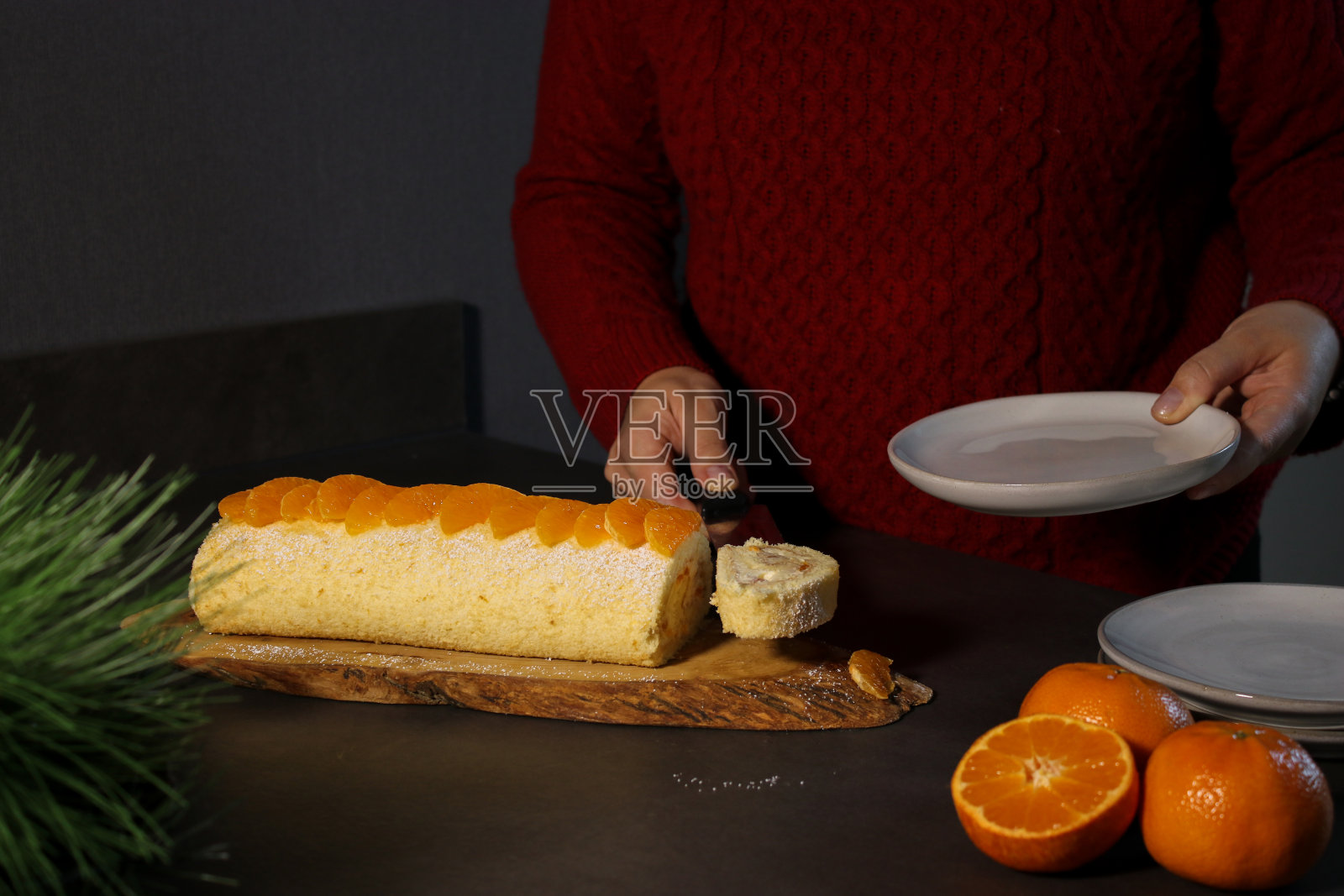 女子端着一盘宁静的橘子蛋糕卷，里面有香草奶油，这是节日的冬季甜点照片摄影图片