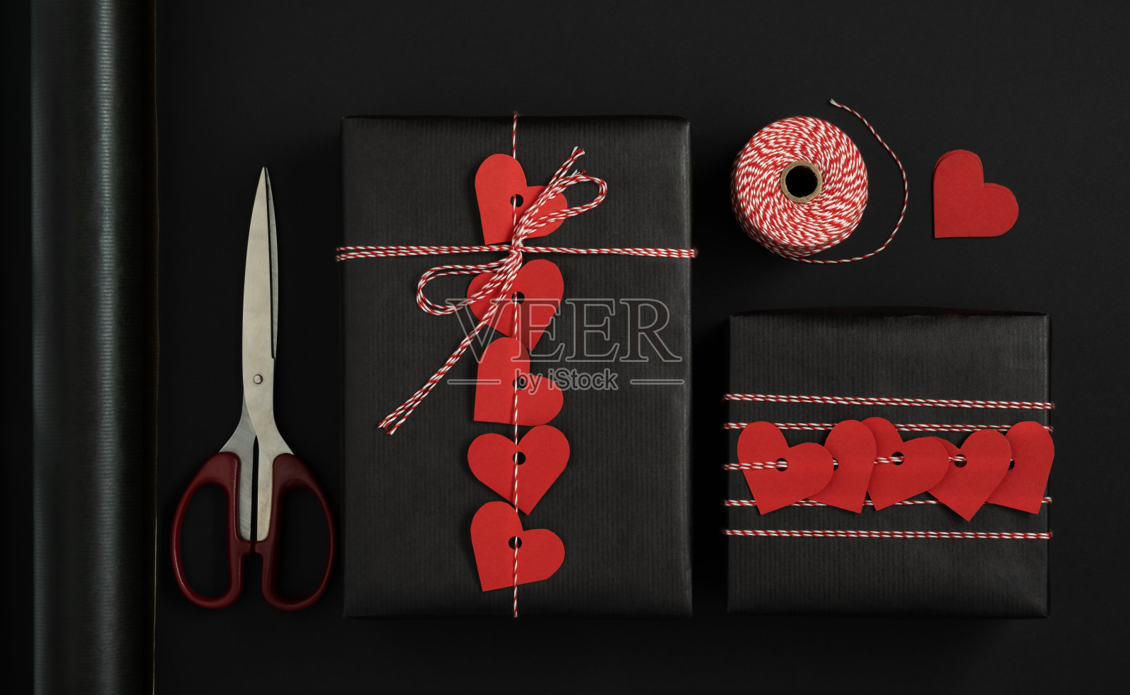 为情人节包装礼物的物品。黑色包装纸，红色心形纸，绳子，剪刀。黑色背景。照片摄影图片