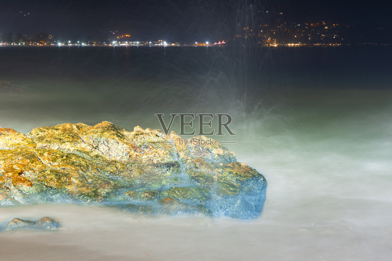 在泰国普吉岛芭东海滩上，长时间暴露在色彩斑斓的夜晚，海浪冲击着岩石照片摄影图片