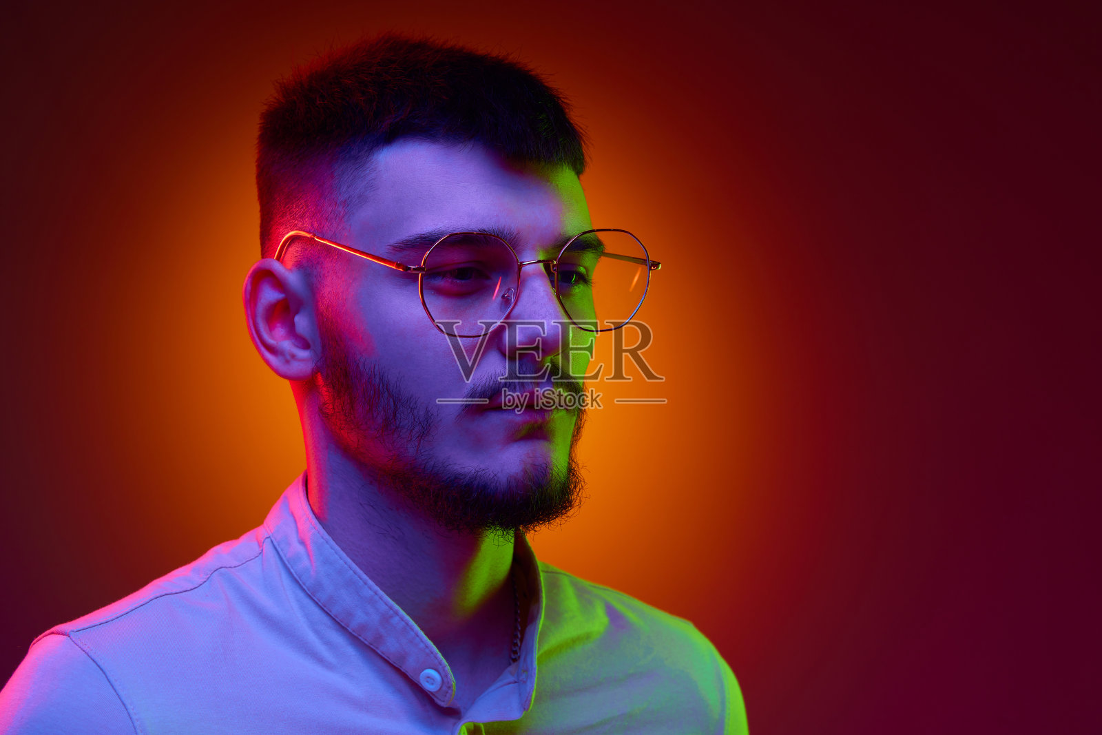 侧视图肖像冷静英俊的年轻人，学生戴眼镜对紫红色背景在混合色光，滤镜。照片摄影图片