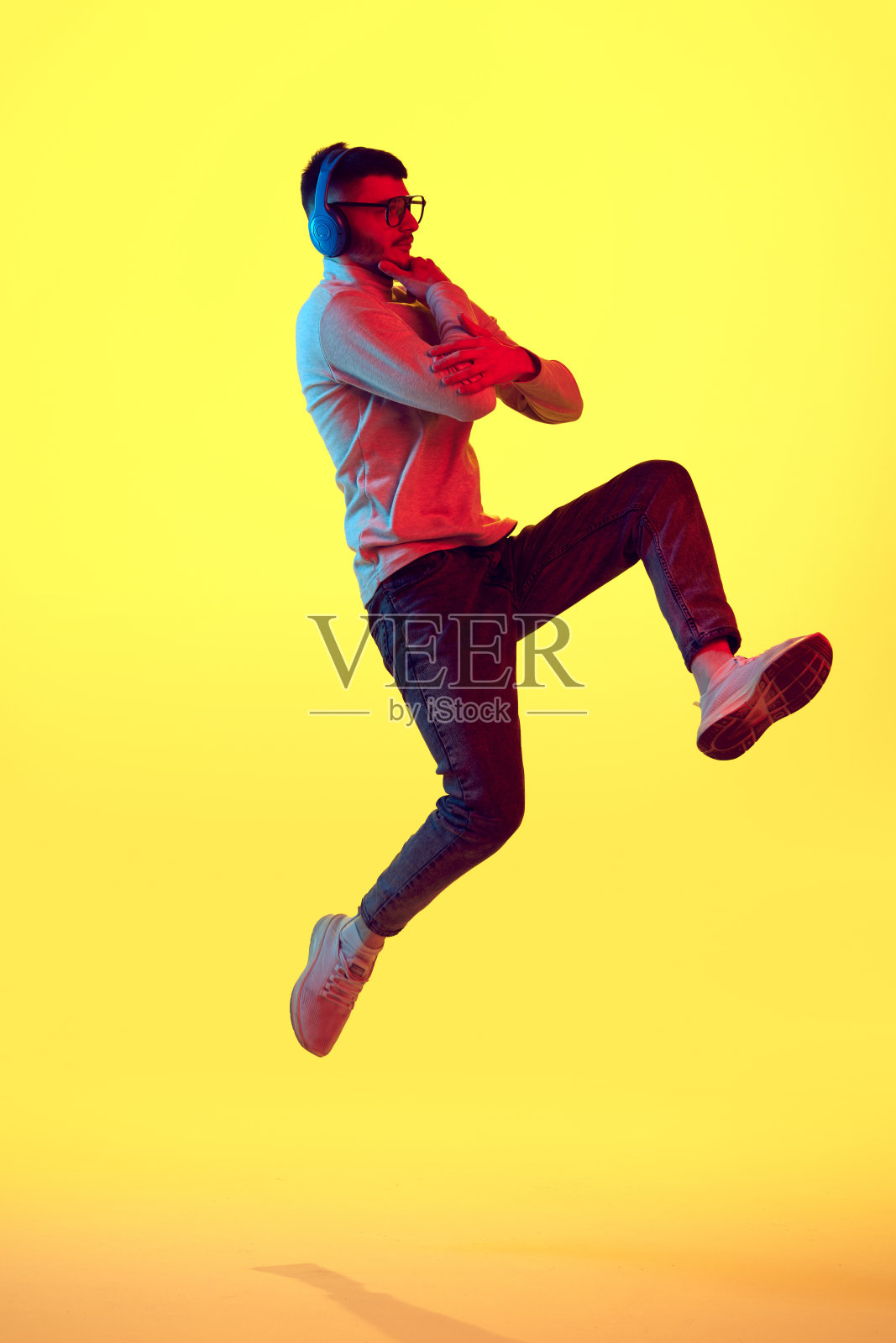 思考的年轻人戴着耳机听音乐，在黄色的背景上跳跃，红色的光，滤镜。照片摄影图片