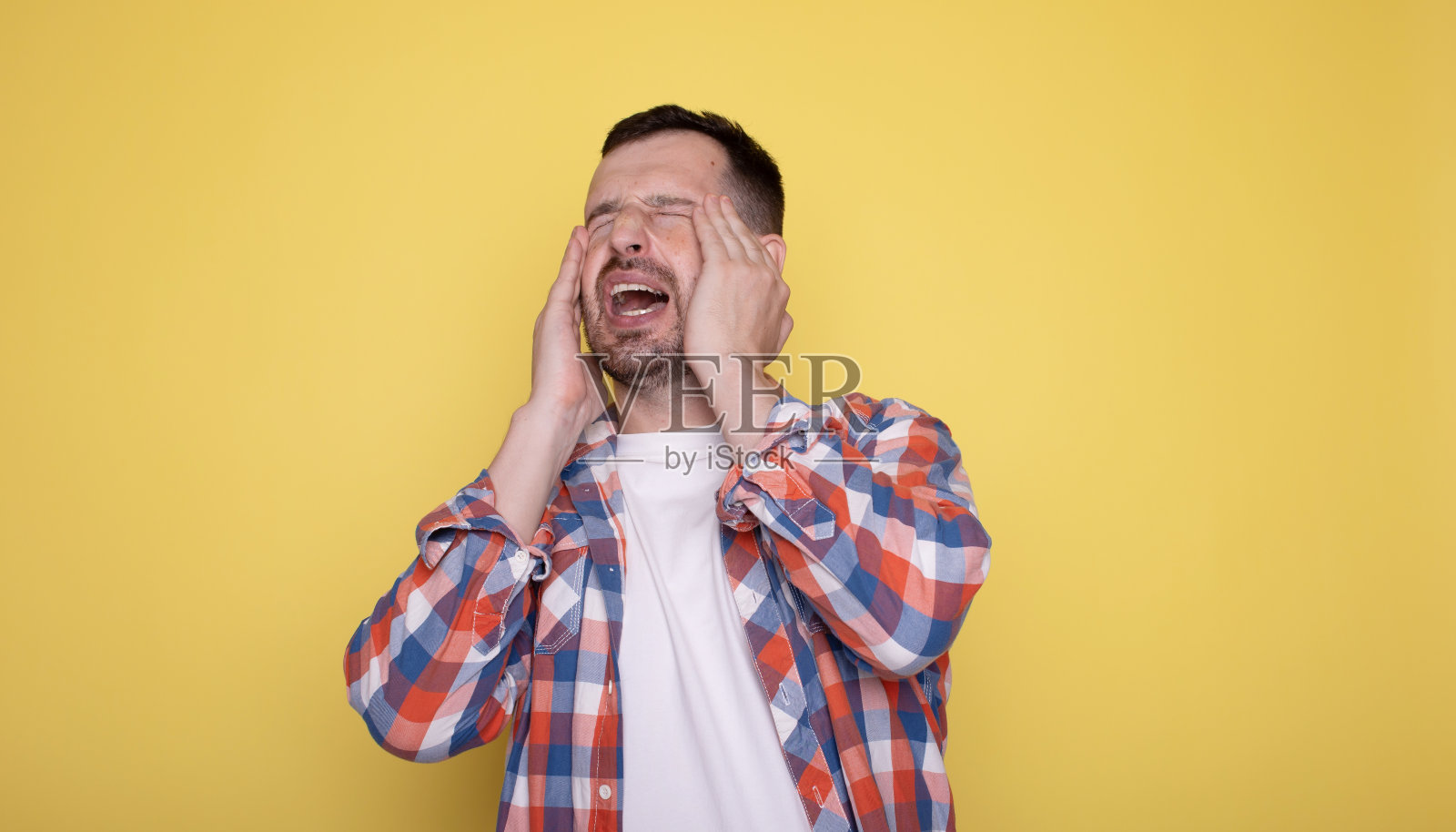 被隔离在黄色背景上的白人男子，头痛，摸着脸的前面。照片摄影图片