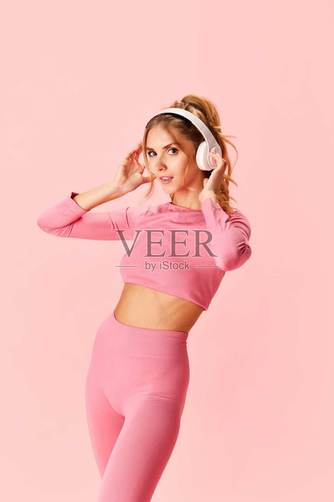 肖像苗条，健康的女人听着音乐，用无线耳机进行有效的锻炼隔离在粉红色的背景照片摄影图片