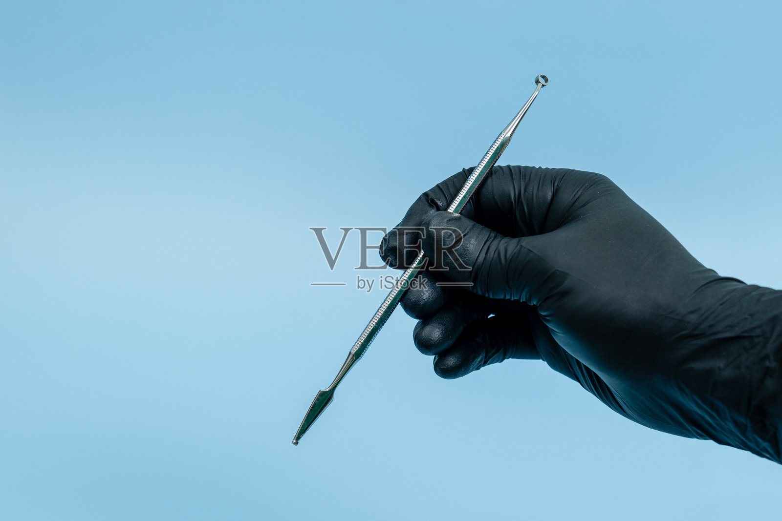 裁剪镜头的专业牙医在黑色医疗手套与牙科工具。牙科的概念。蓝色背景隔离照片摄影图片