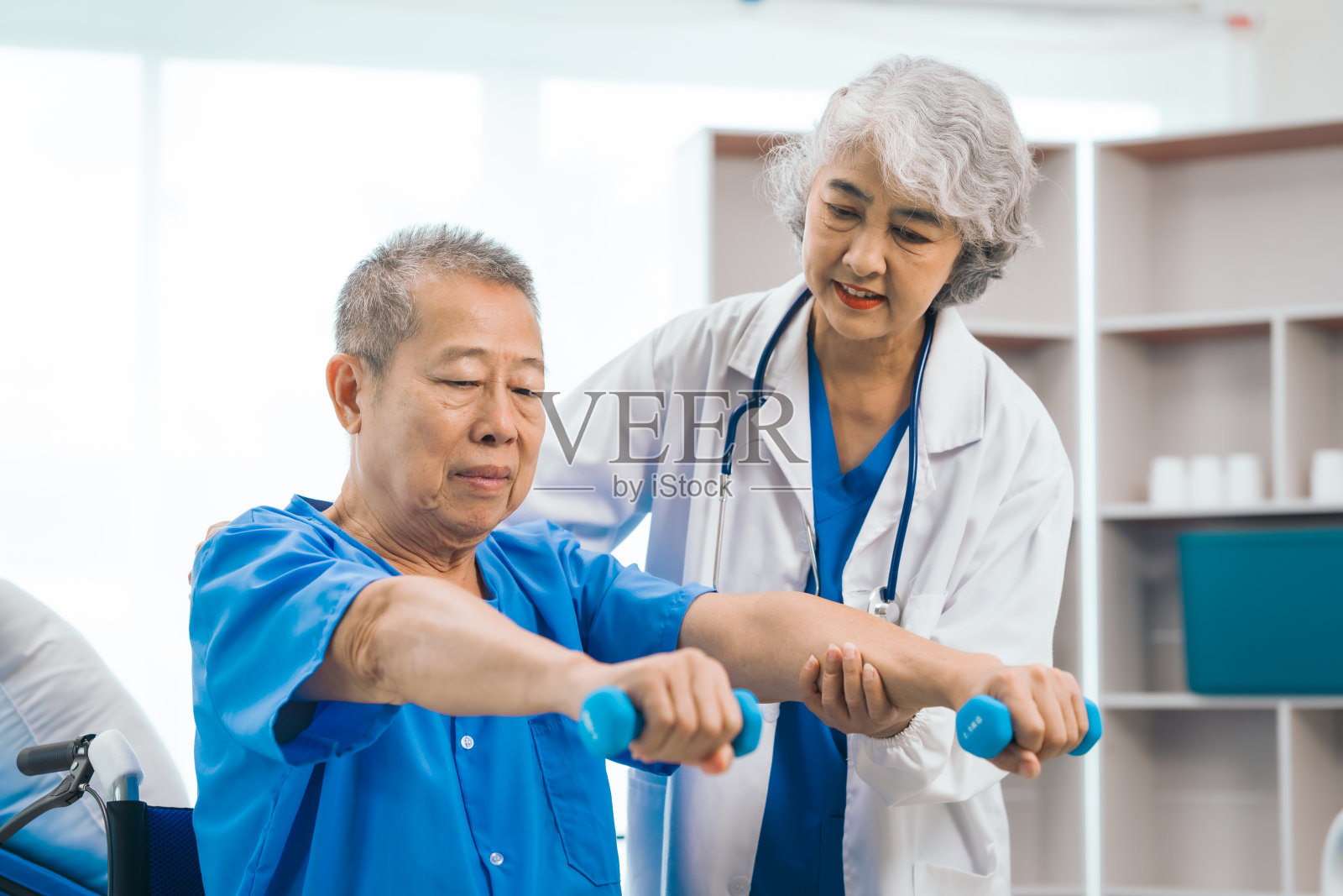 亚洲人成熟的女医生给男性老年患者在保健轮椅上进行室内物理治疗，强调动手支持和康复。专家理疗照片摄影图片