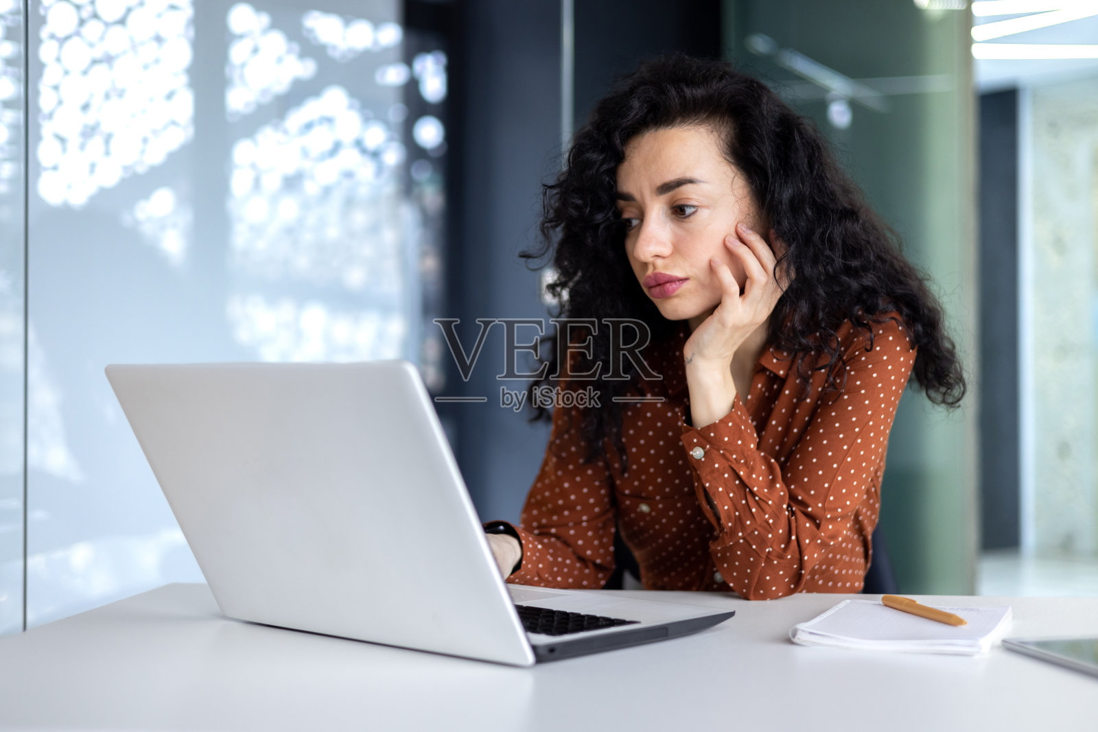 在办公室里认真思考的拉美女性，在工作时用笔记本电脑思考复杂决策的女商人。照片摄影图片