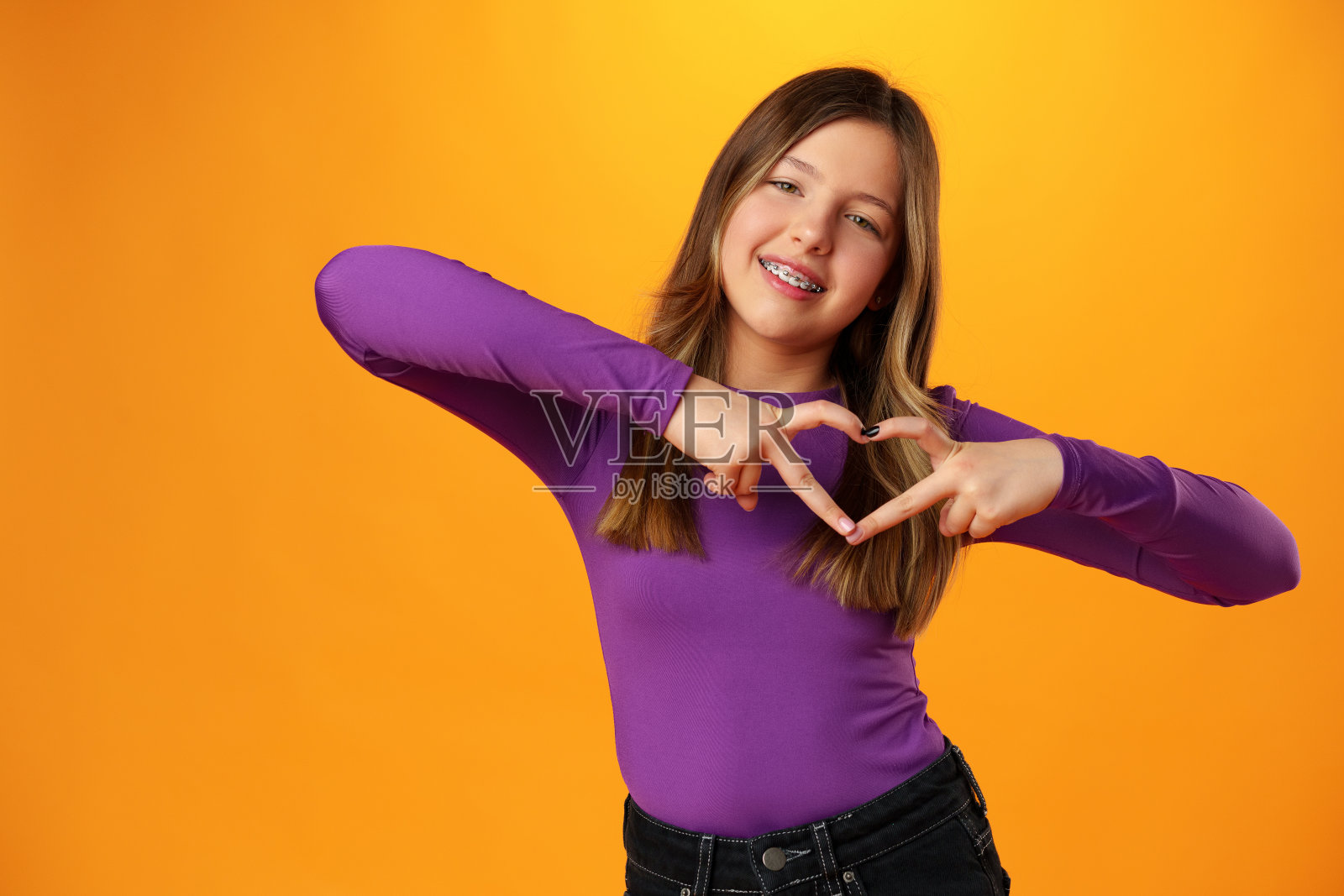 友好的十几岁的女孩在黄色背景上展示了内心的爱照片摄影图片