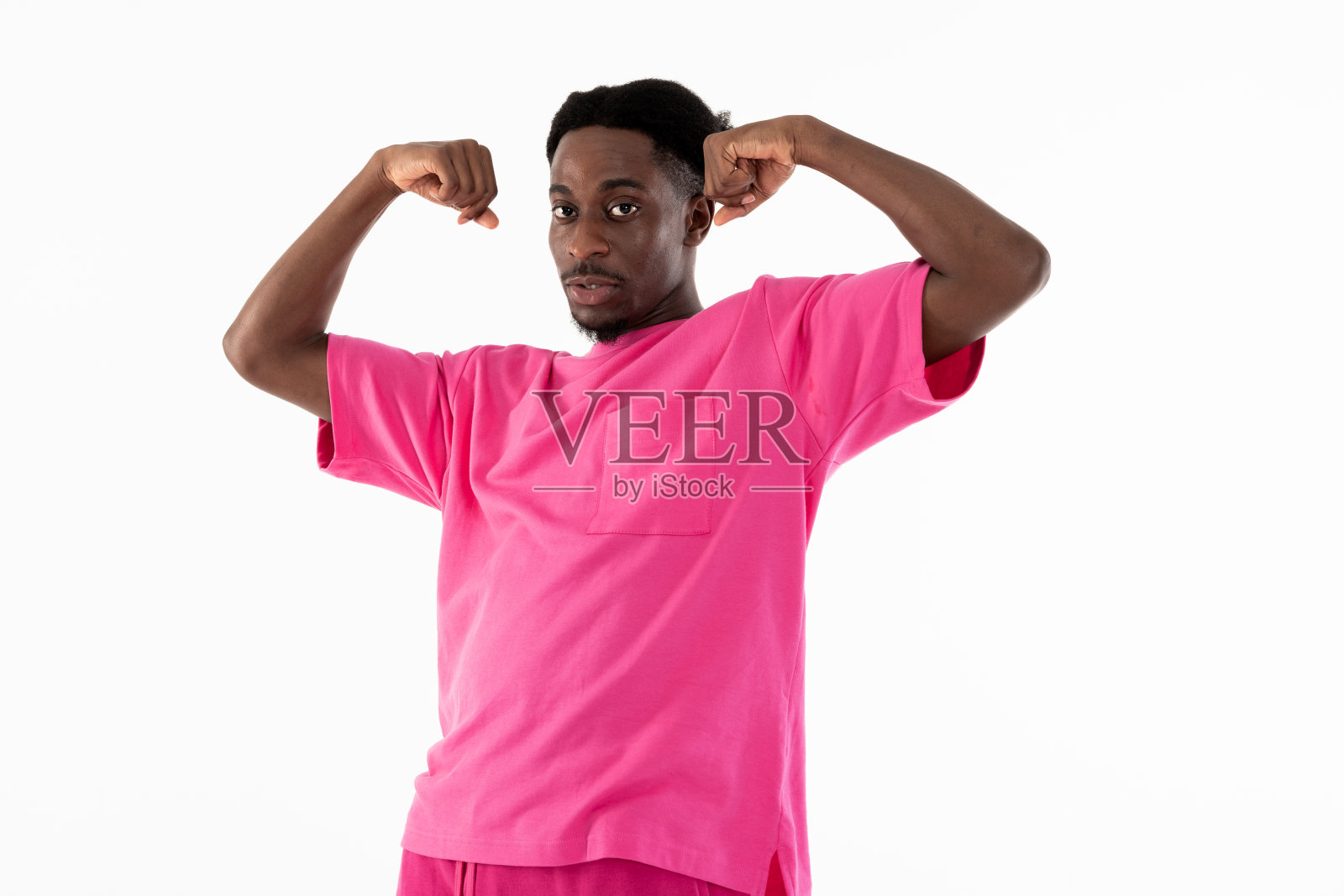 英俊的非裔美国人穿着时尚的粉红色运动服，在镜头前展示二头肌，表达严肃的情绪照片摄影图片