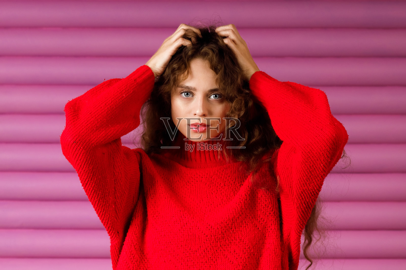卷毛微笑的年轻成年女子穿着冬天的红色毛衣抚摸着头发看着镜头。照片摄影图片