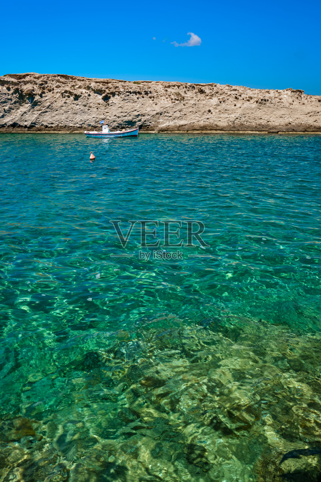 停泊在希腊国旗下的小渔船，碧蓝的海水，碧蓝的天空，岩石嶙峋的小山，红色的捕鱼浮标漂浮着。额。米洛斯岛,希腊。照片摄影图片