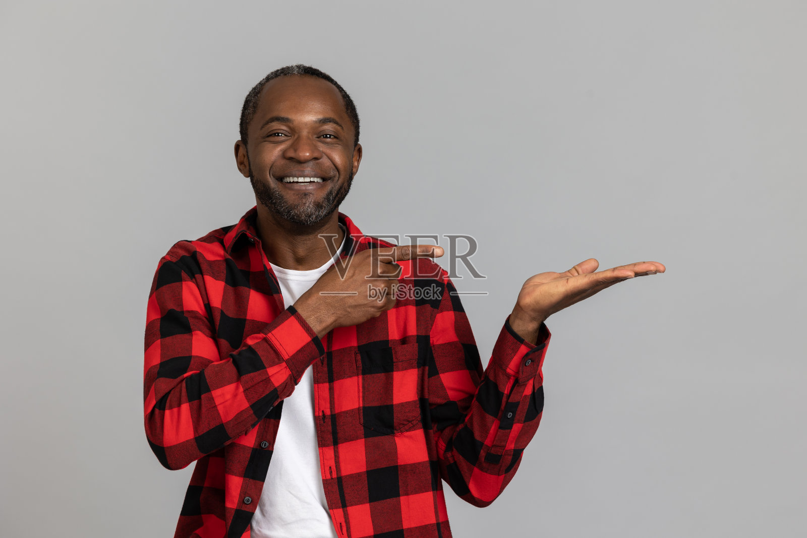 穿着红色格子衬衫的快乐黑胡子男子指着手掌上的广告区域照片摄影图片