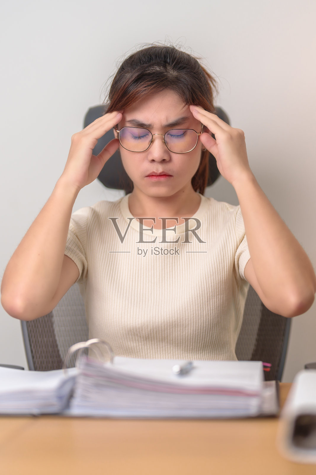 在办公室头痛和偏头痛的女商人，在工作中感到疲惫和压力的亚洲女性，在家里拿着一叠文件到深夜的疲惫女性。过度工作和加班照片摄影图片