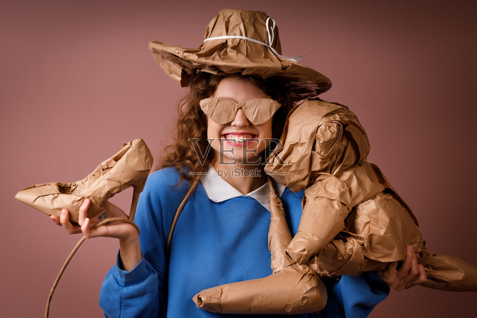 年轻的积极微笑的女人收到惊喜的礼物，手里拿着一束用质朴的米色工艺纸包着的礼物。帽子，鞋子，吹风机，毛绒玩具和眼镜。照片摄影图片