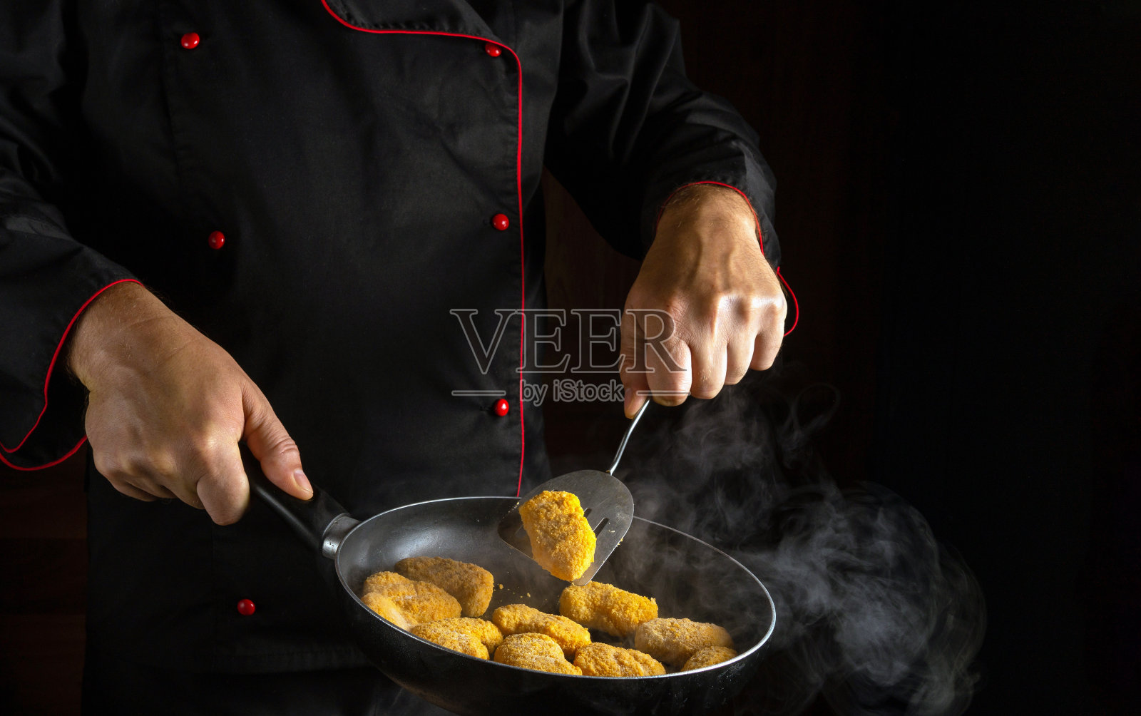 烹饪酥脆的鸡块。厨师在烟雾缭绕的热锅里翻炒土豆。一个有广告空间的酒店的大厨房的想法照片摄影图片