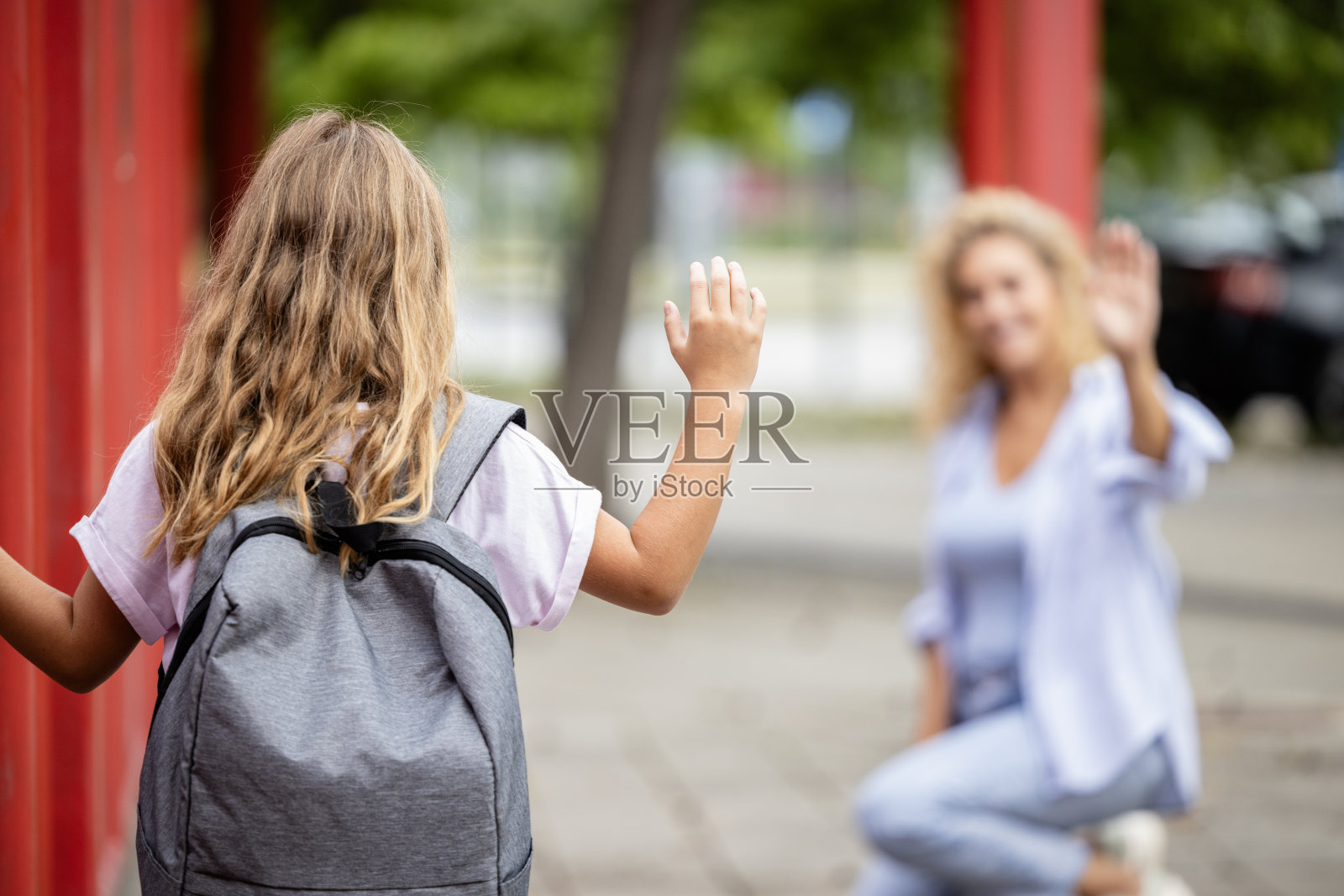 背着书包的女学生在进学校时向妈妈挥手。一位家长扶着孩子第一天上学。照片摄影图片