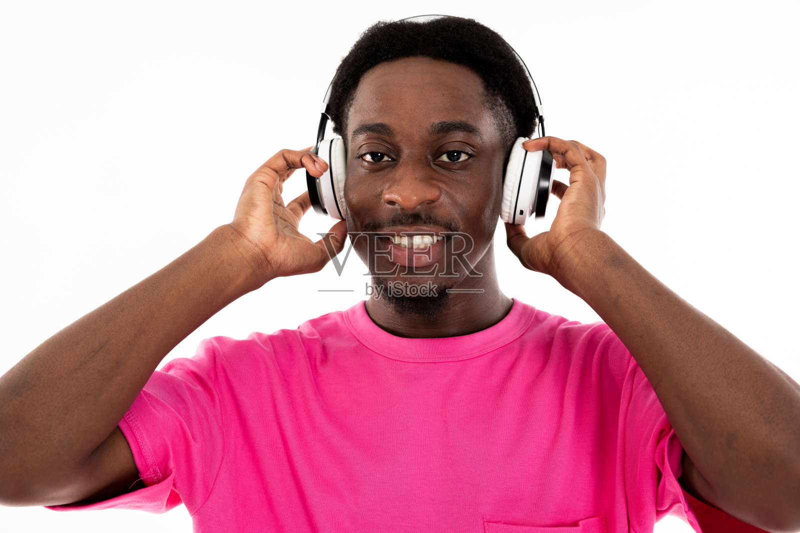 微笑的非洲裔美国人的肖像，戴着耳机，看着相机，听着白色背景的音乐，在工作室里为广告拍摄过程摆姿势照片摄影图片