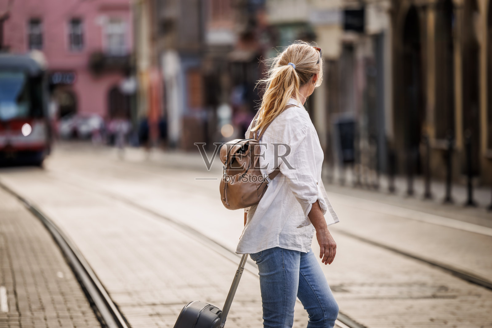 一个带着行李箱的旅行者穿过有电车轨道的街道照片摄影图片