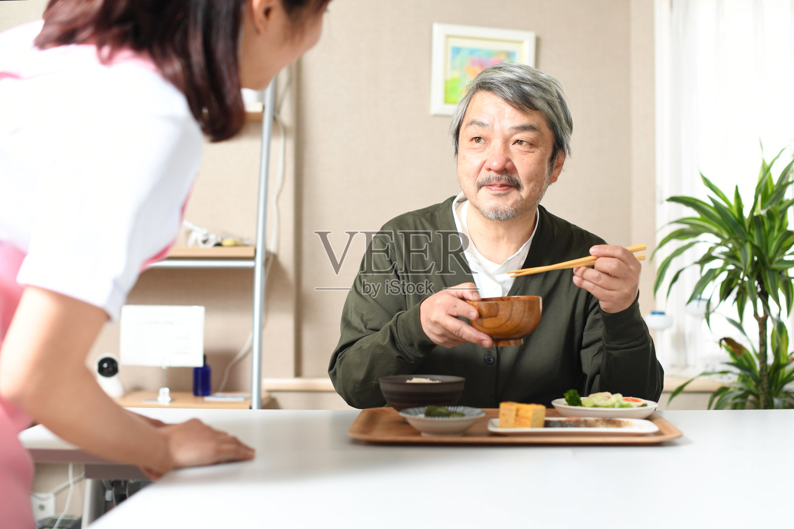 一位女护工正在帮助一位白发苍苍的亚洲老人做饭。照片摄影图片