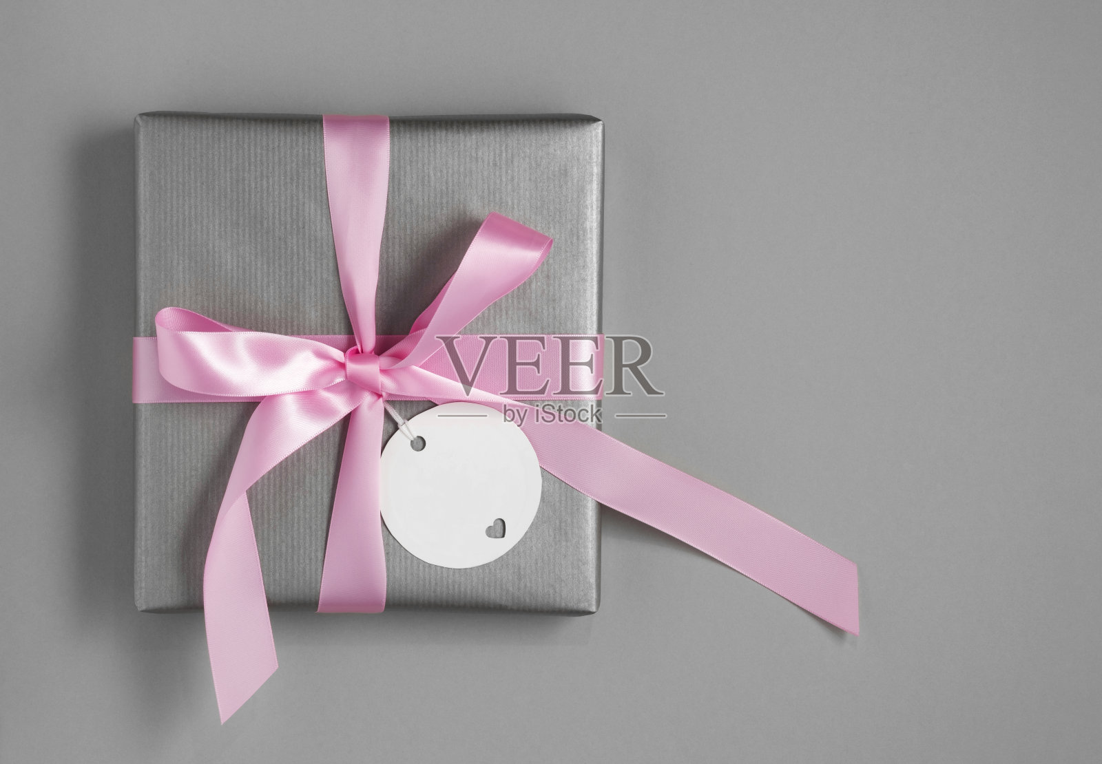 银色礼盒与粉红色缎带和白色空礼品标签在灰色背景。为你的文字留出空间。照片摄影图片