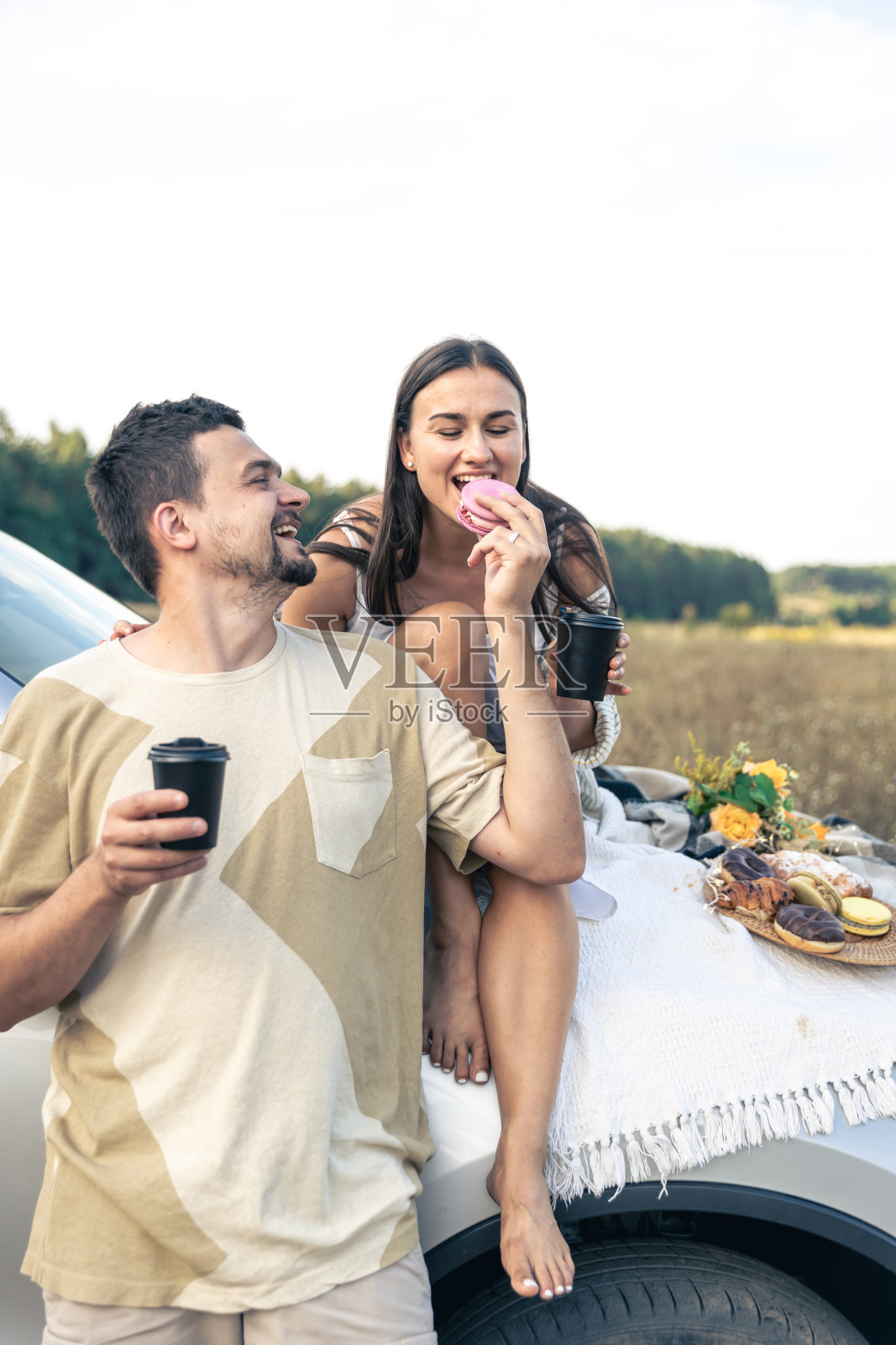 一对夫妇站在越野车旁边，在日落的草地上享受野餐时光。照片摄影图片