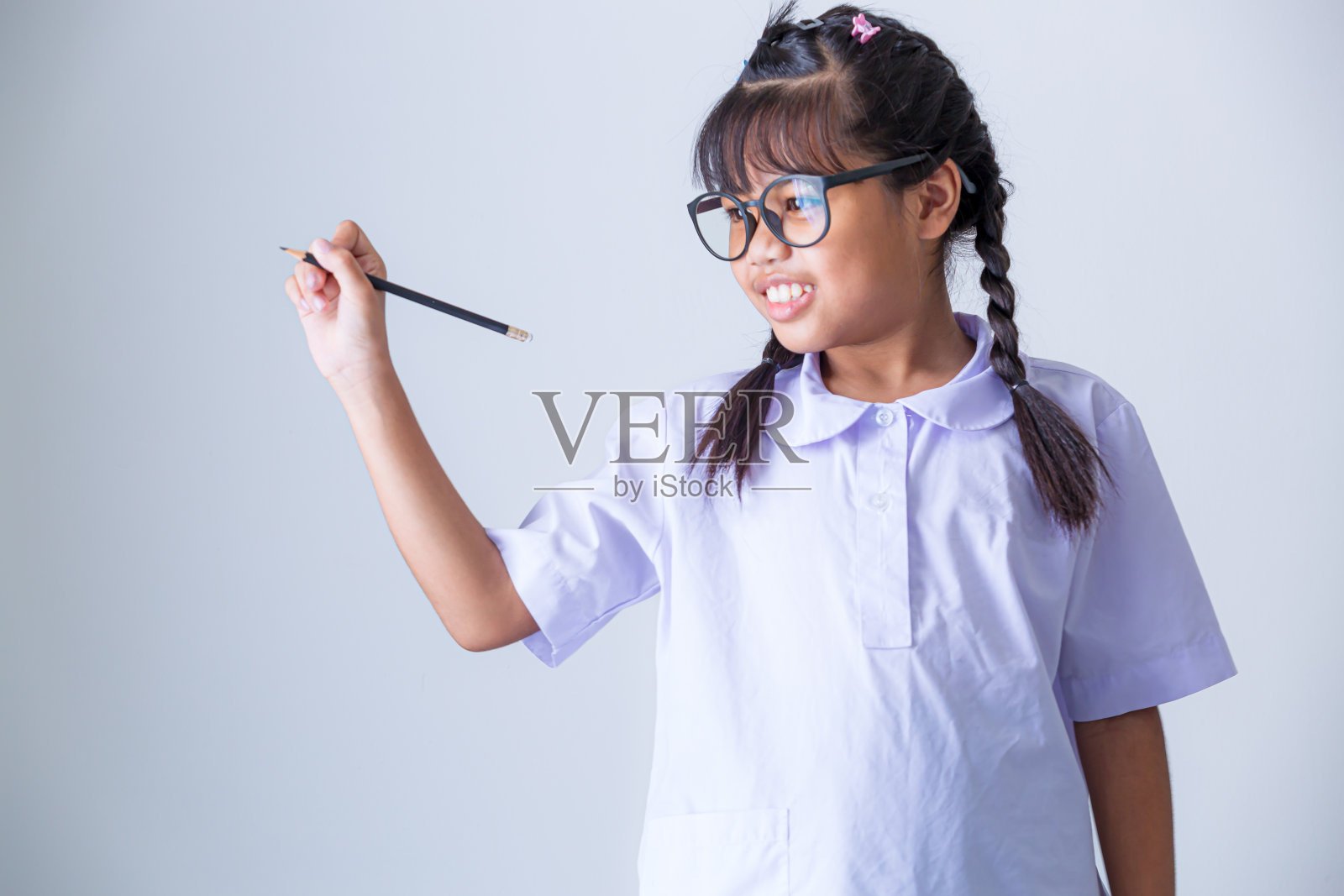 穿着泰国校服的女孩，肖像可爱的亚洲学生女孩，穿着泰国校服，手指向上指向孤立的粉红色背景。照片摄影图片