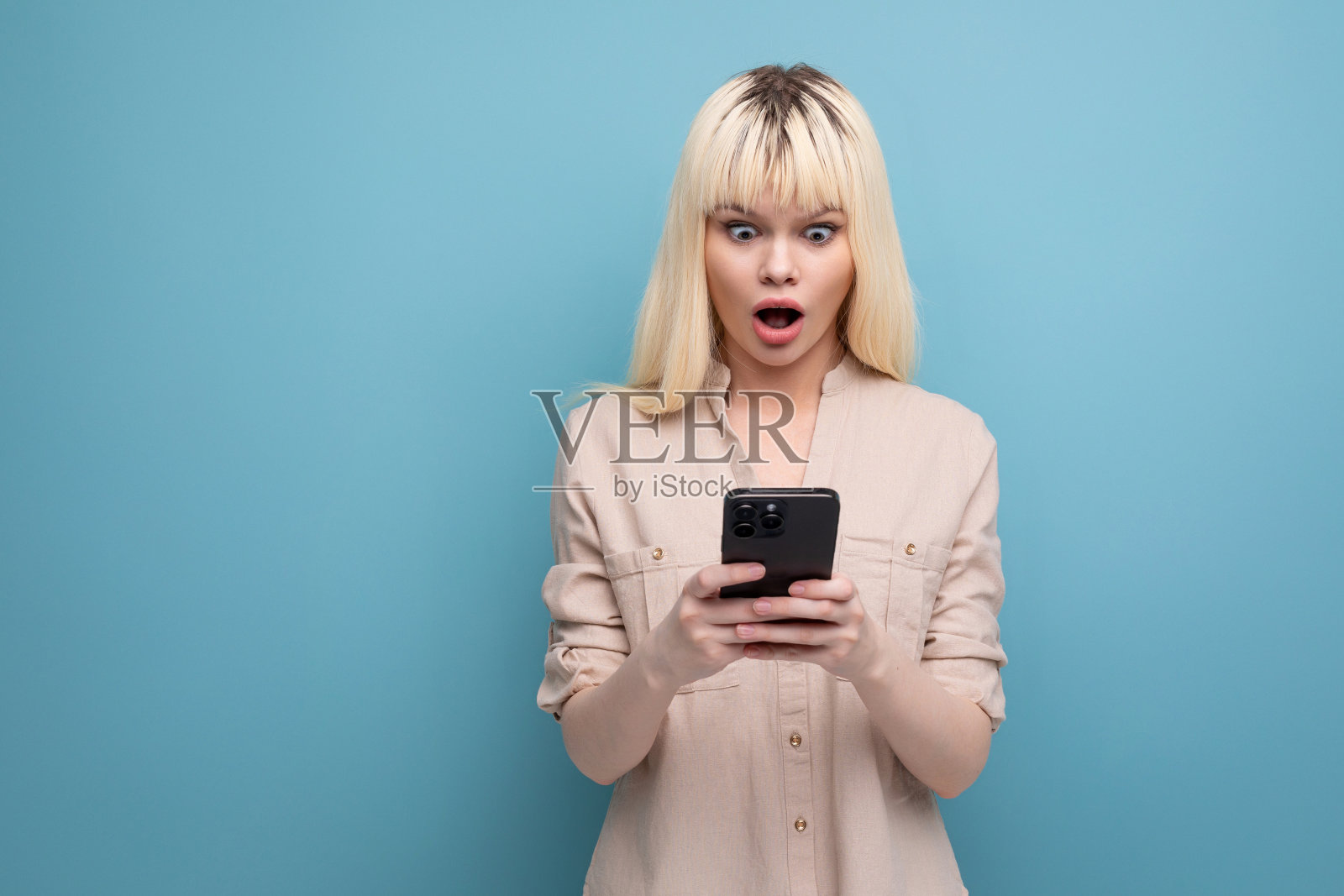 惊讶的金发年轻女子拿着智能手机照片摄影图片