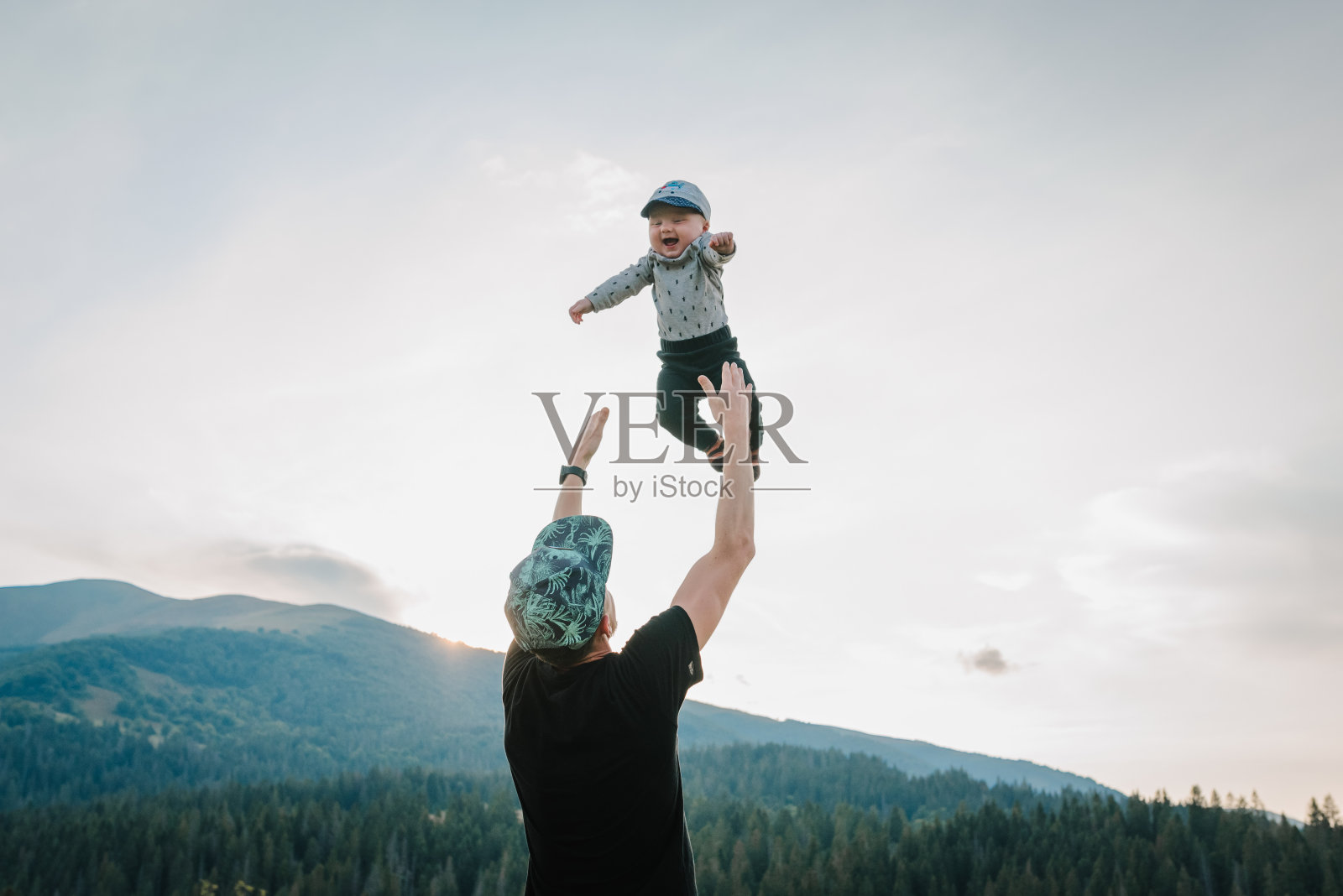 父亲用双手把他快乐的儿子抛向天空。秋日漫步大自然。爸爸和小宝宝在山上玩耍。家人一起度假的概念。照片摄影图片