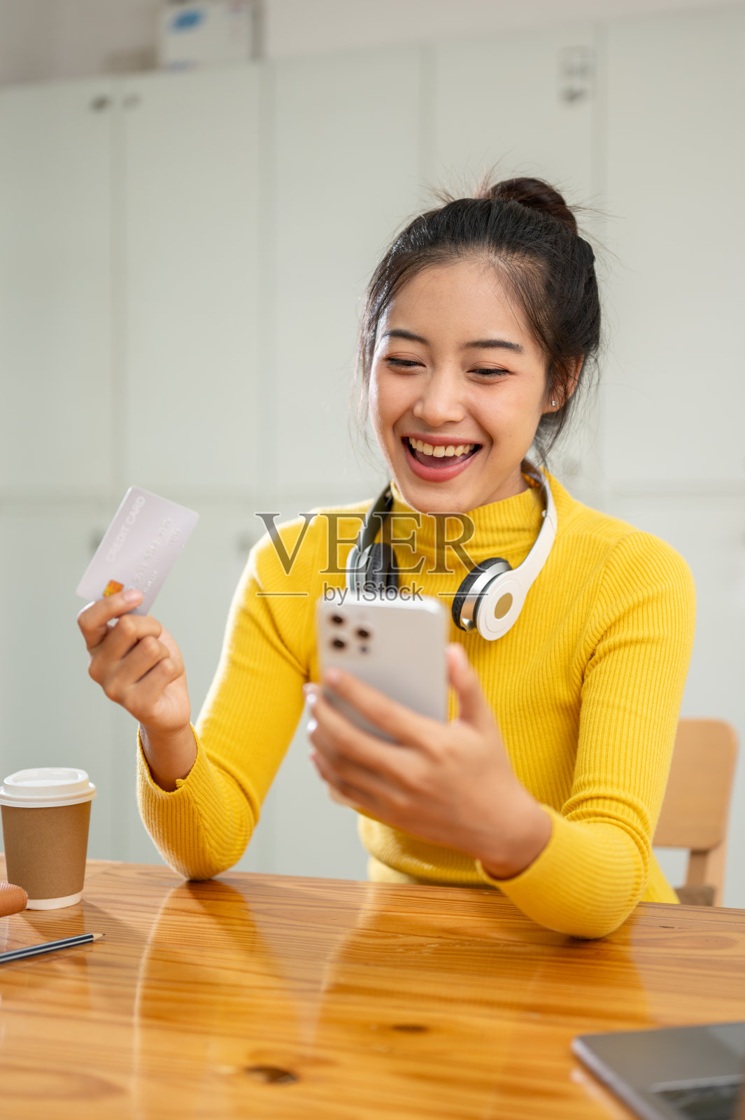 一位快乐的亚洲女性拿着信用卡和智能手机，正在享受购物应用程序照片摄影图片