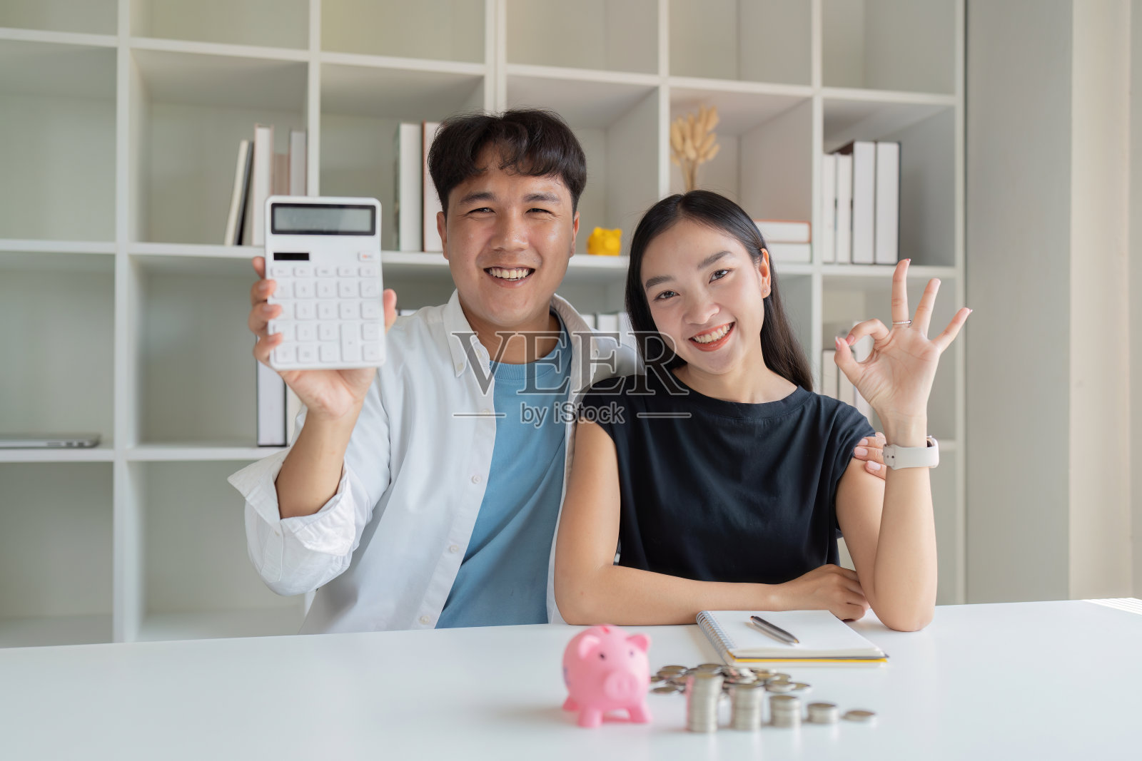 年轻夫妇对投资、理财计划充满信心，女人拿出OK的手势，男人拿出计算器照片摄影图片