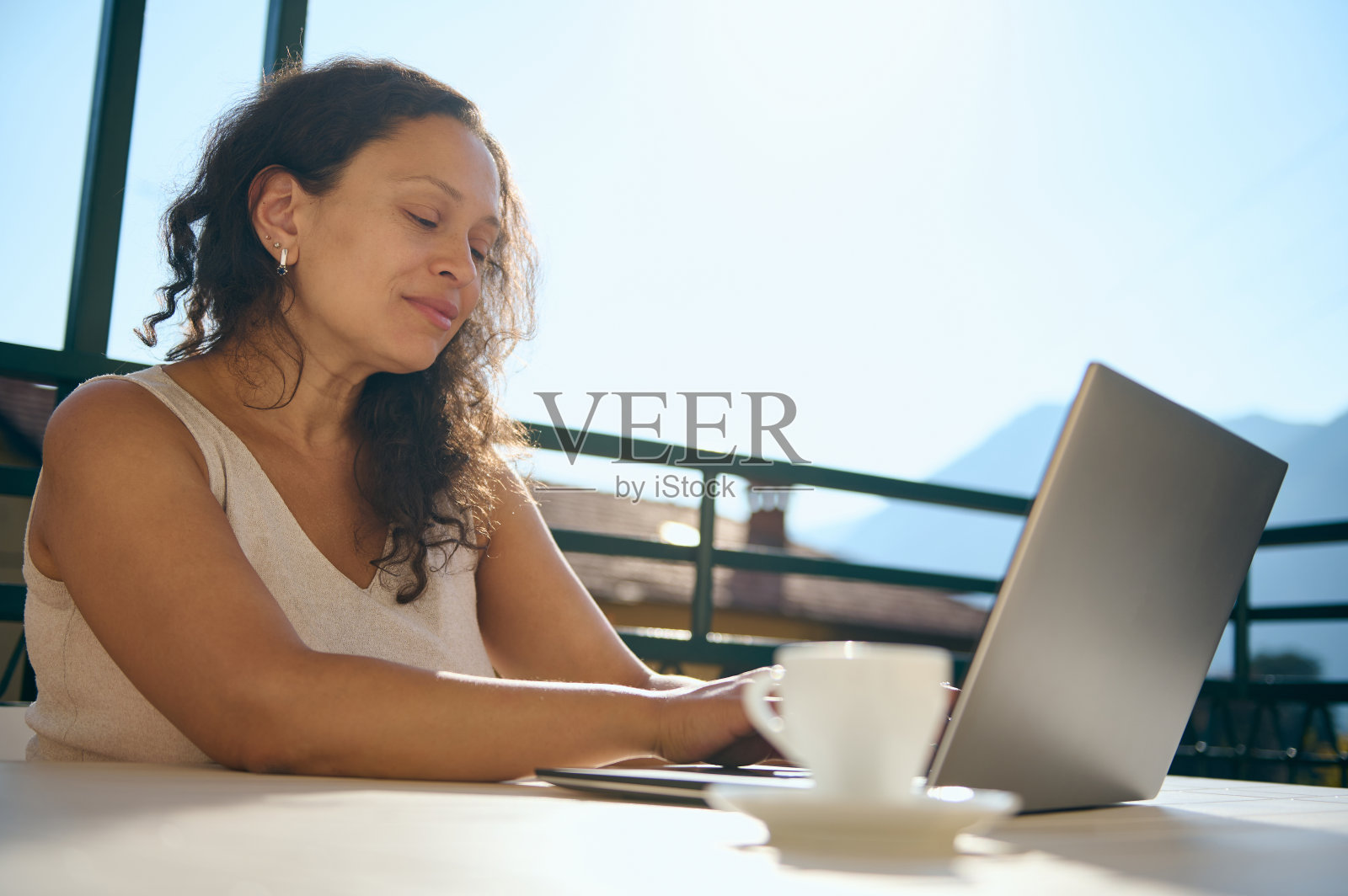 成熟的女性企业家，使用笔记本电脑，远程工作，端着咖啡杯坐在桌子旁的女商人照片摄影图片