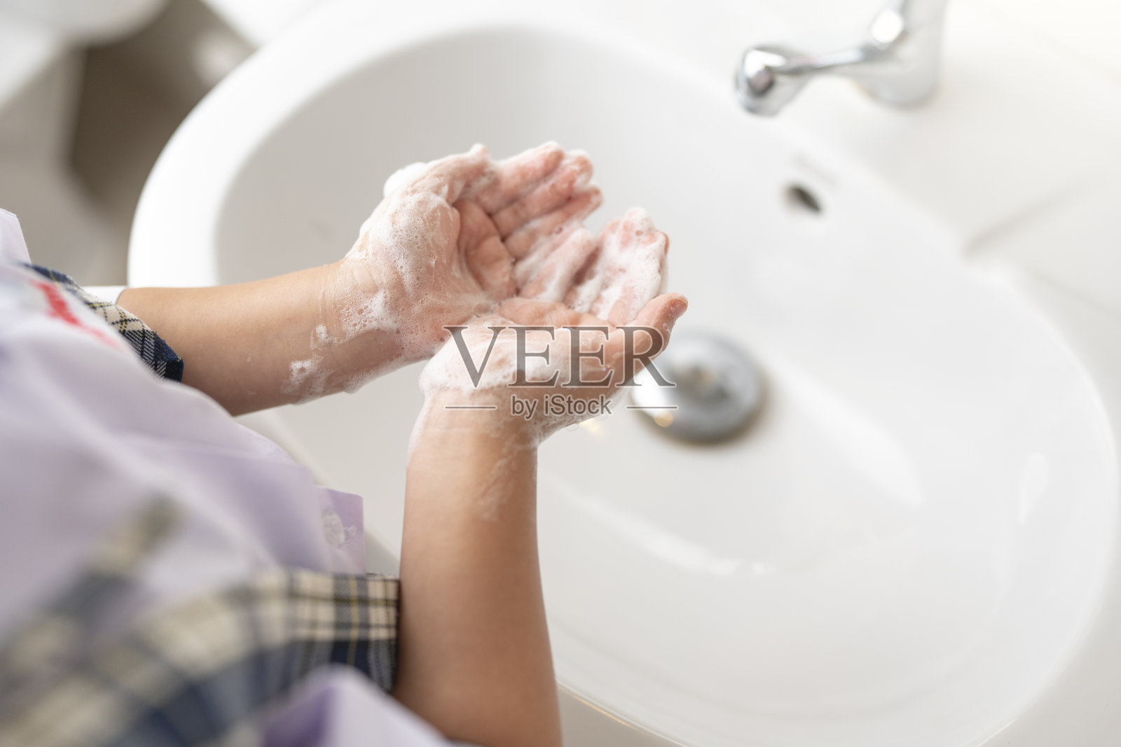 穿着校服的小女孩在水池边用泡沫肥皂洗手。照片摄影图片