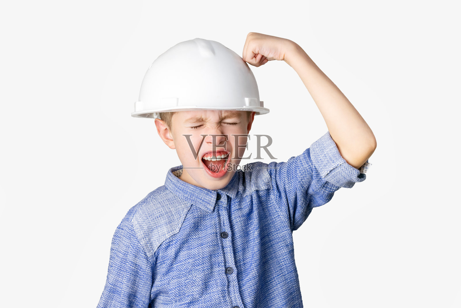 一个戴着白色安全帽的男孩笑着用拳头打他的头盔。情绪化的孩子笑着，眯着眼睛，张着嘴。乐趣、梦想、童年、想象。照片摄影图片
