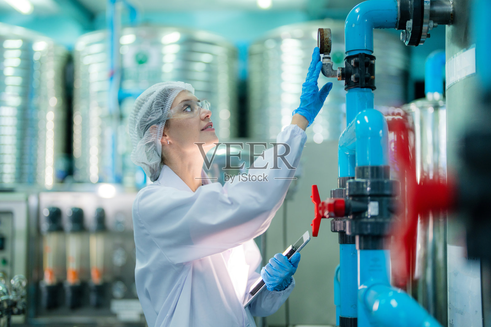 工业工厂的科技工人在检查反渗透机系统的质量。女工在控制面板上记录数据，测量便携式回收装置的压力。照片摄影图片