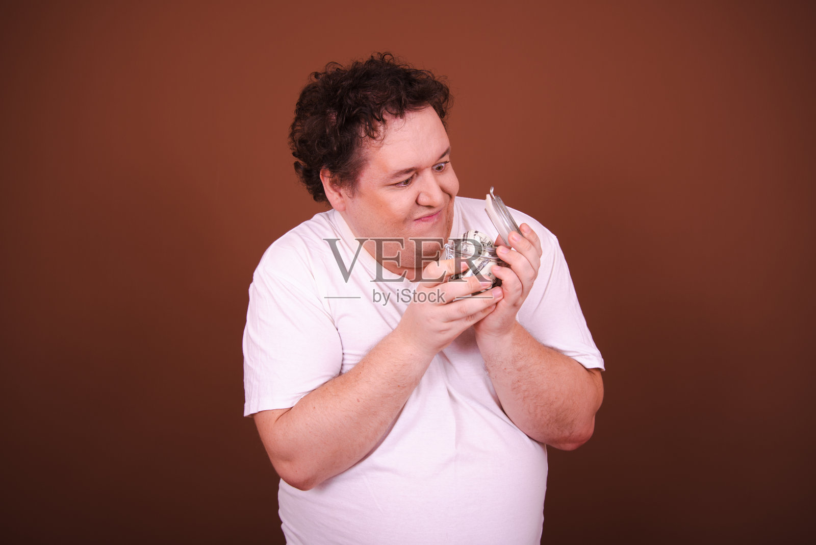 有趣的胖子在存钱。男人有强烈的情感。棕色的背景。照片摄影图片