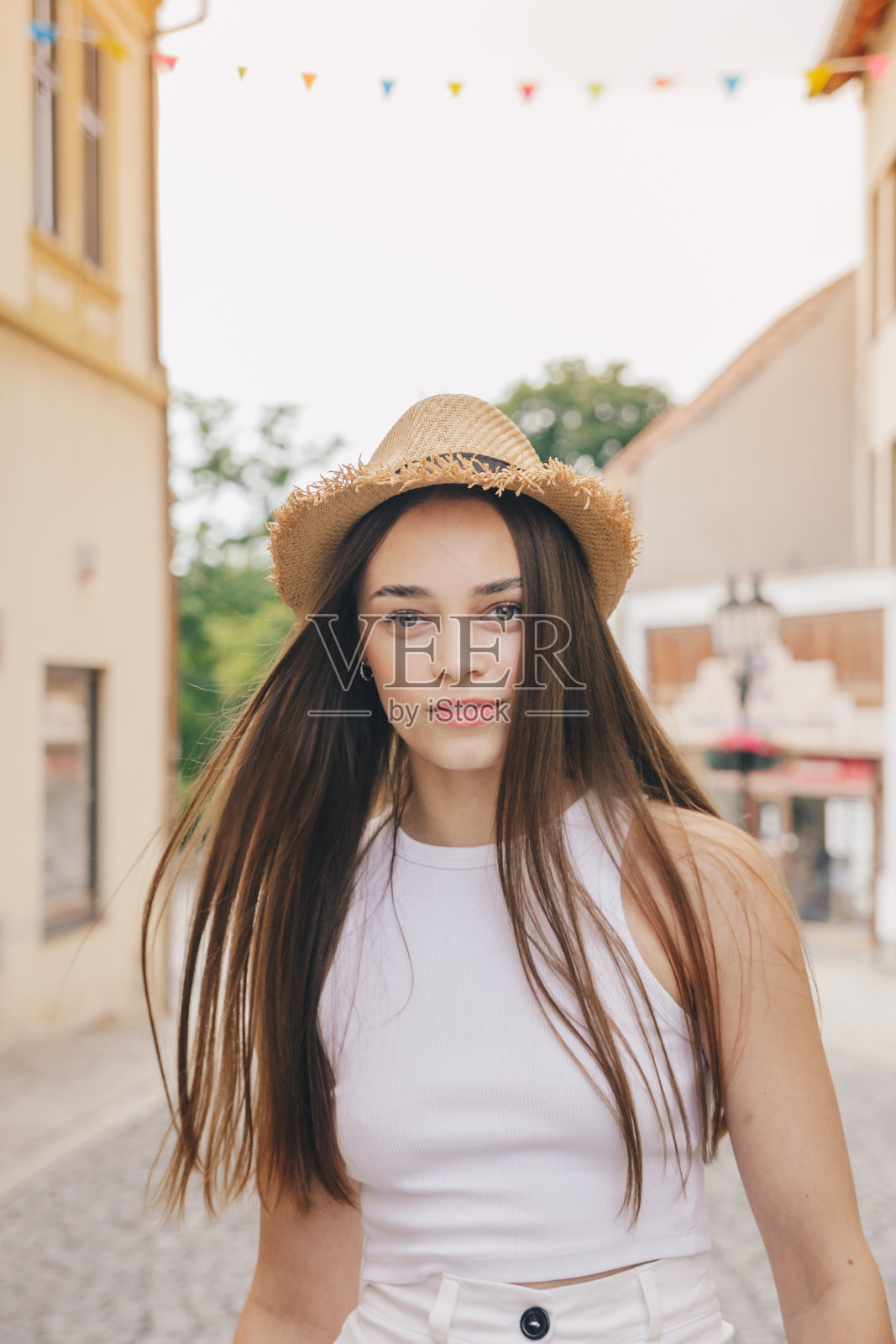 美丽的白人女孩，一头白色长发，戴着漂亮的帽子，在欧洲的街道上散步。垂直照片，社交网络概念。照片摄影图片