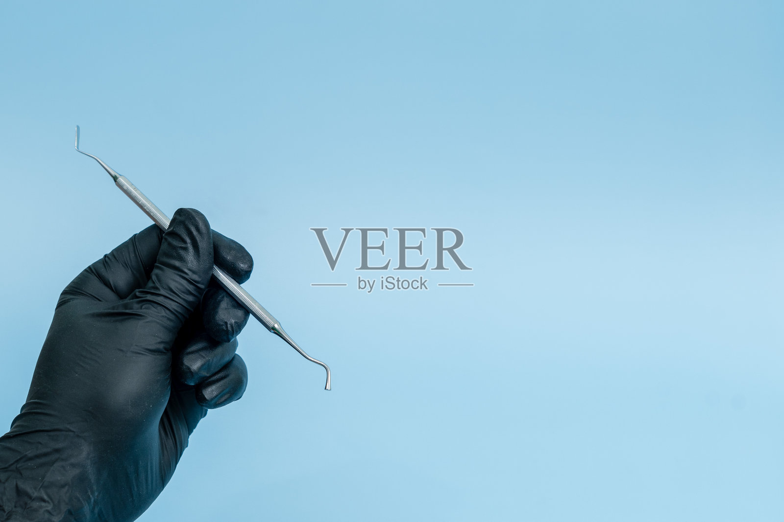 裁剪镜头的专业牙医在黑色医疗手套与牙科工具。牙科的概念。蓝色背景隔离照片摄影图片