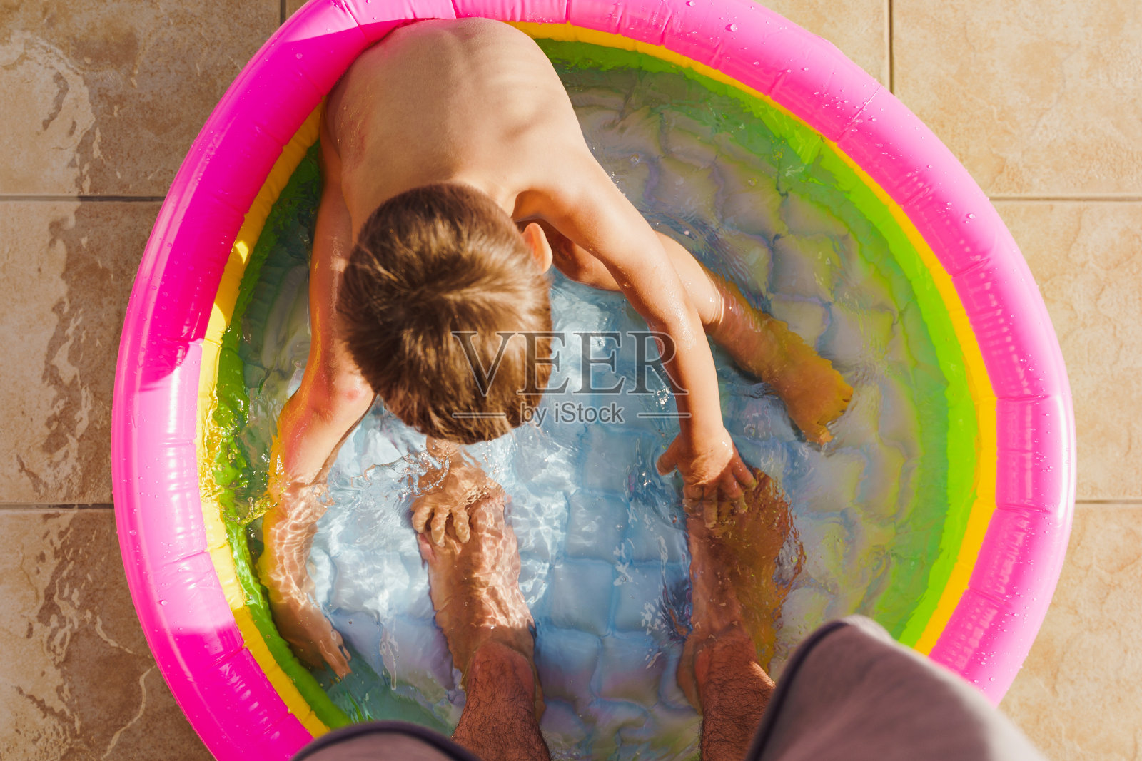蹒跚学步的小男孩在父亲脚边的充气圆形游泳池里玩耍照片摄影图片