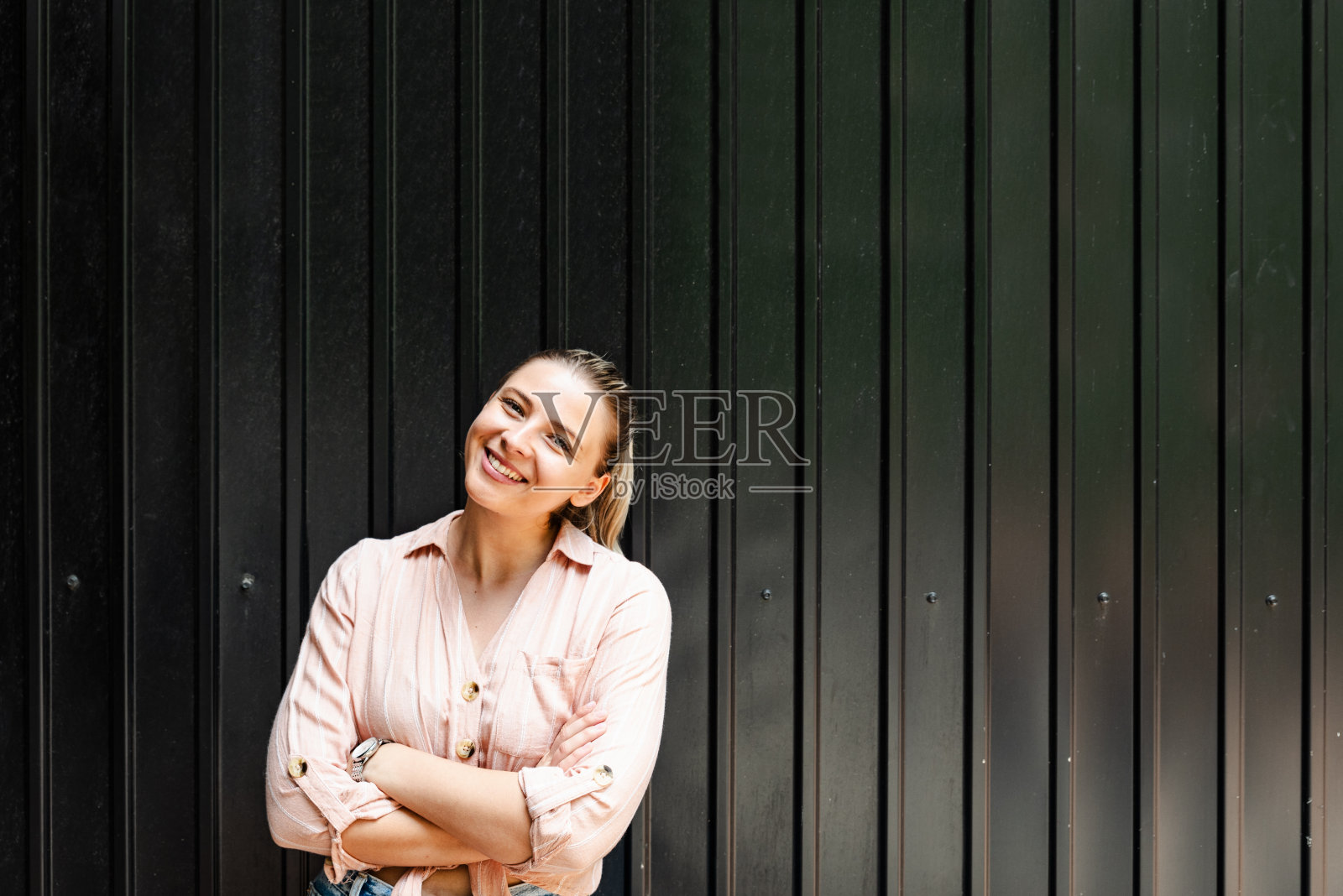 美丽的年轻自信的坚强独立的女人站在自然光线下摆姿势，用黑色的墙做背景。幸福生活的女性肖像照片摄影图片