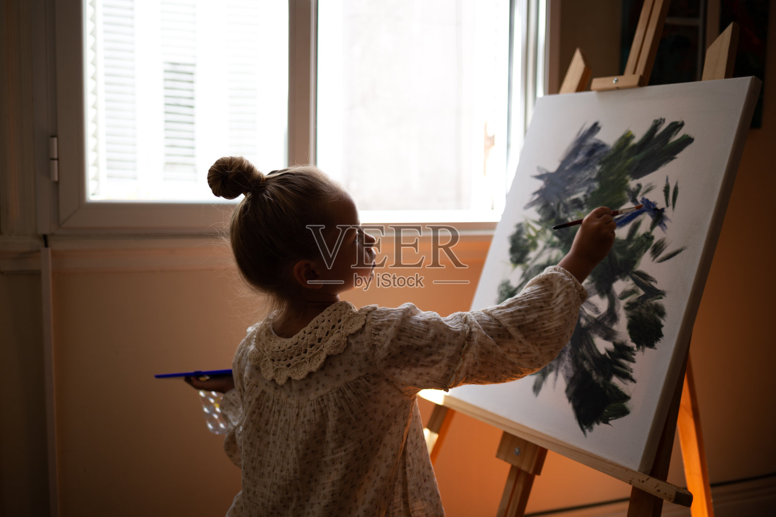 女孩在画架前的画布上画画。早期开发儿童才能的概念。照片摄影图片