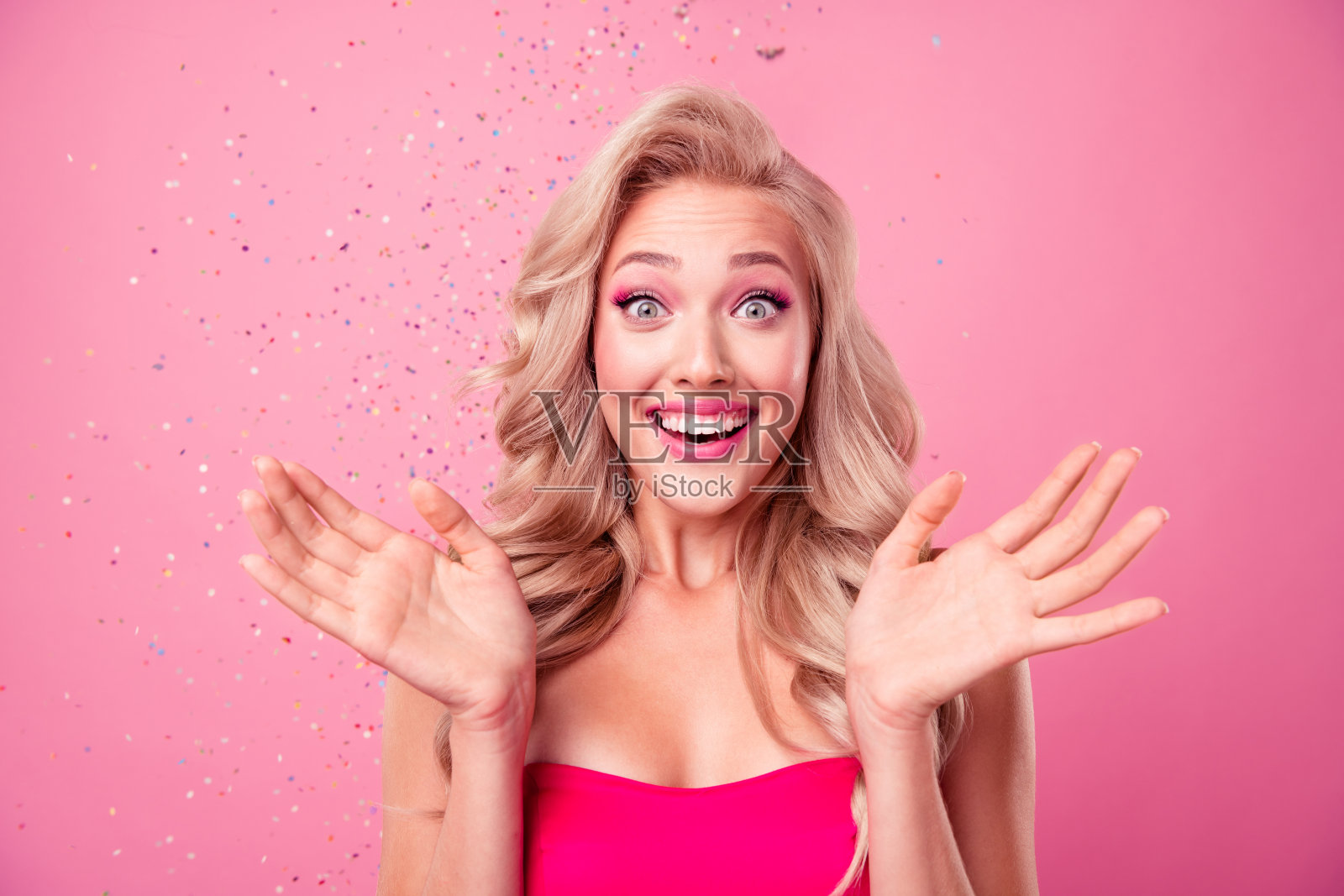 惊讶的快乐的人的肖像举起张开的双臂，手掌灿烂的微笑飞纸屑孤立在粉红色的背景照片摄影图片